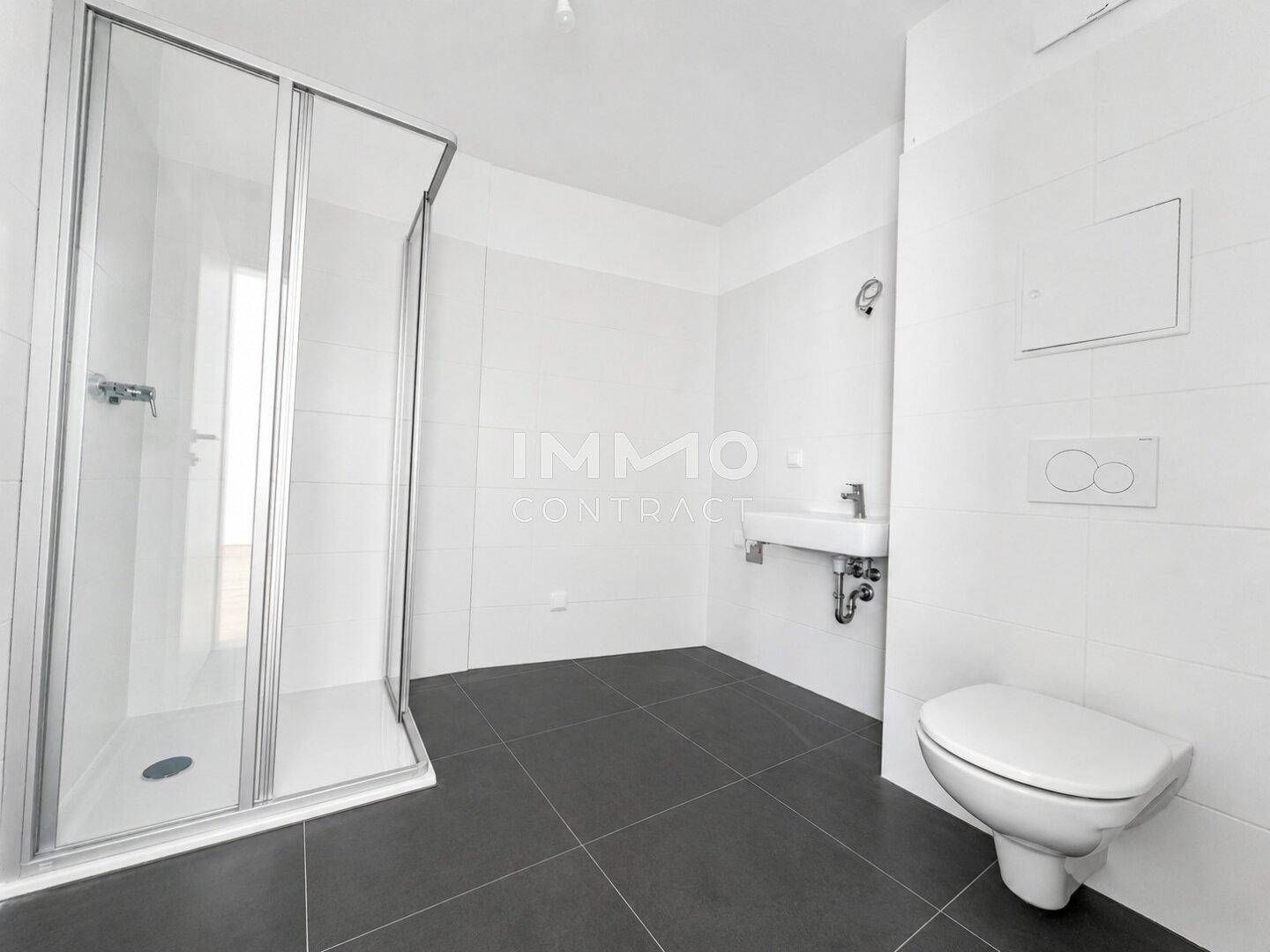 Modernes Badezimmer mit Duschkabine, Wand-WC, Waschbecken und dunklen Bodenfliesen.