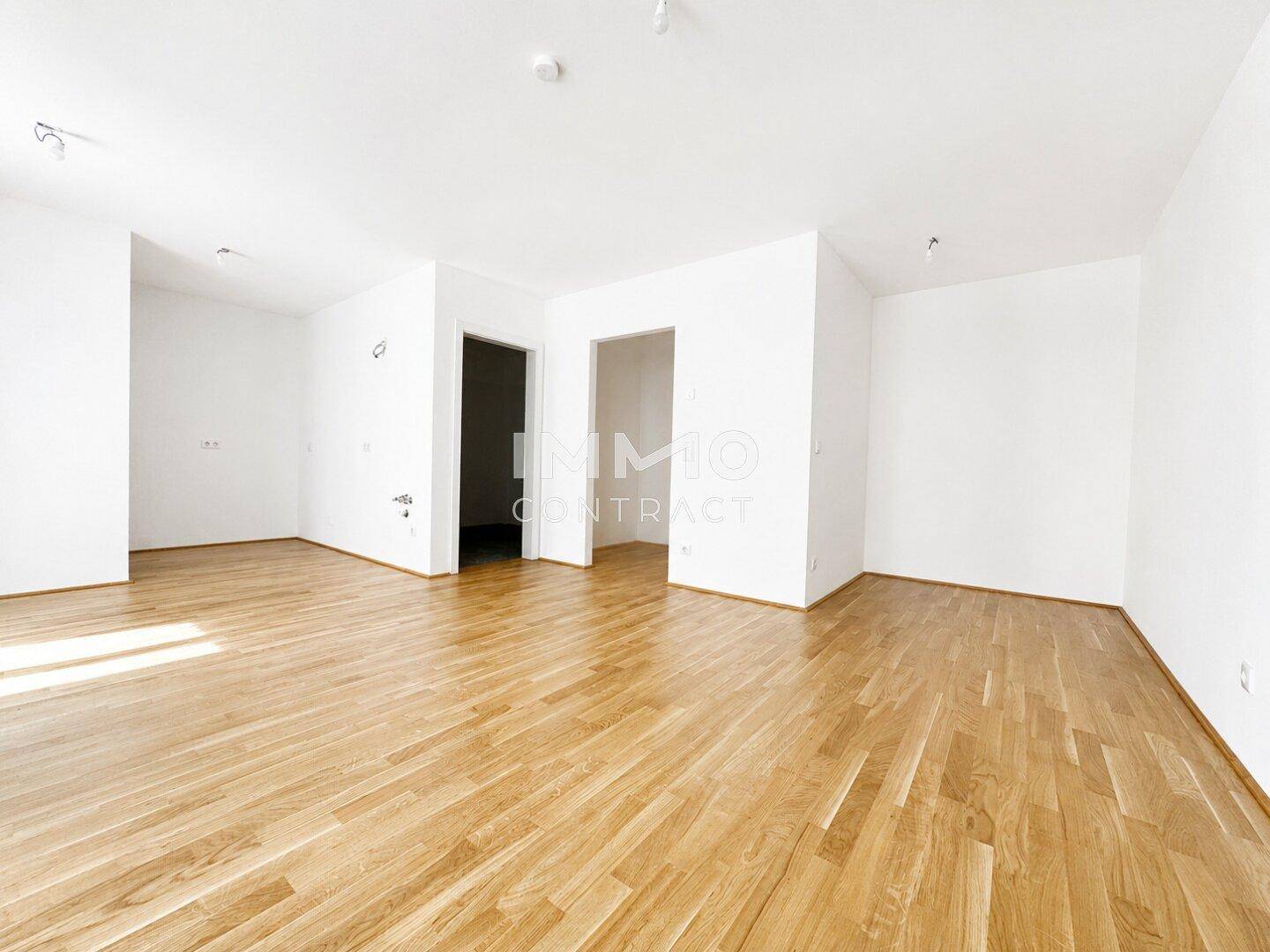 Geräumiger, heller Raum mit Parkettboden und weißen Wänden in einem Neubau.
