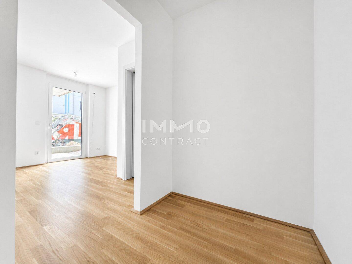 Heller Raum mit Parkettboden und Zugang zu einem Balkon oder einer Terrasse.