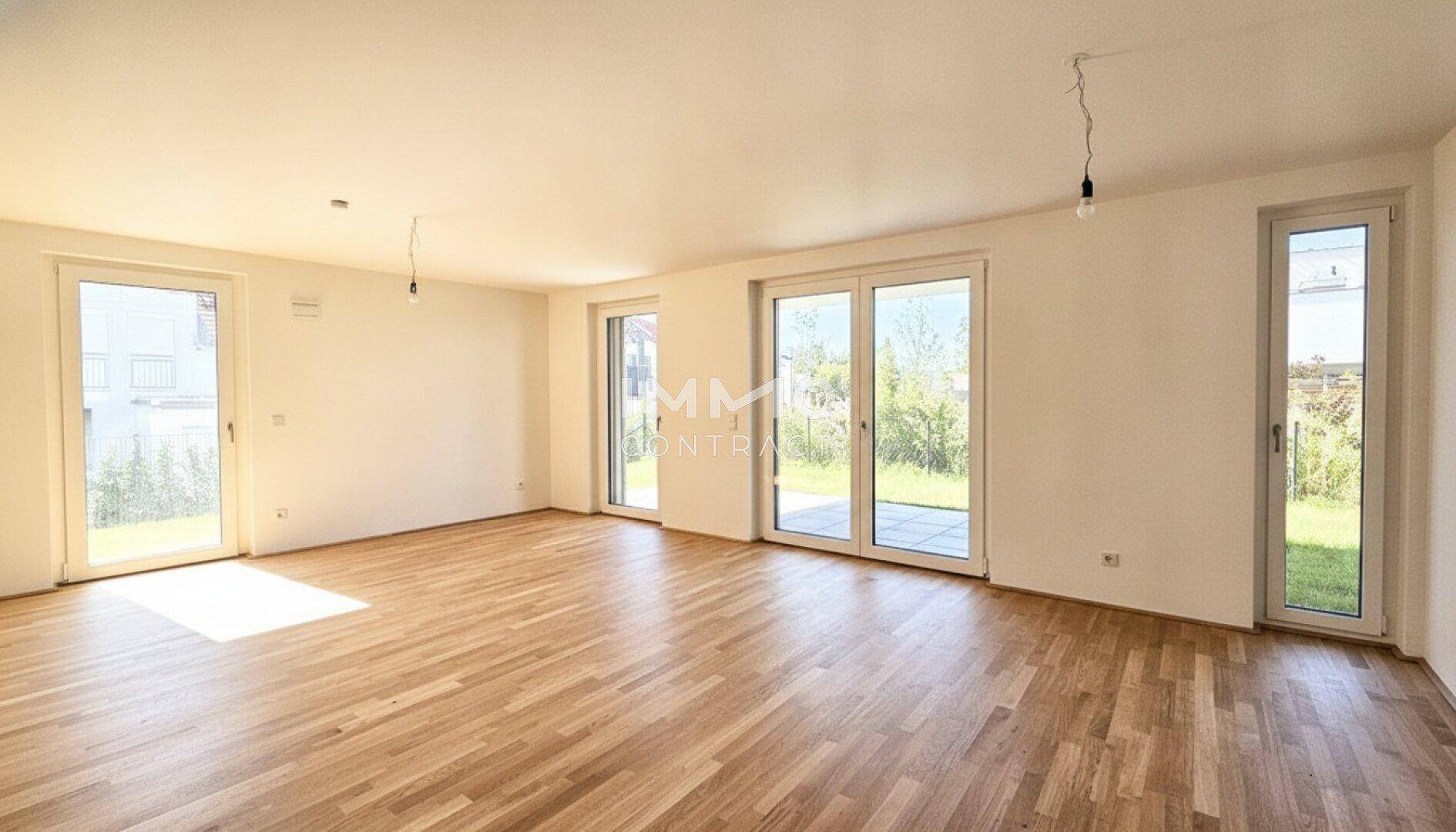 Heller, leerer Wohnbereich mit Holzboden und Zugang zum Garten durch große Fenster.