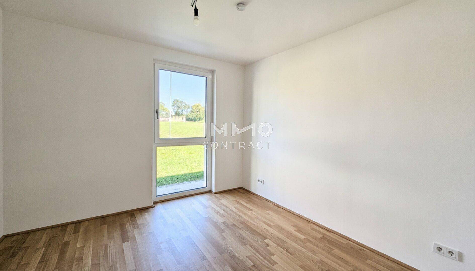 Helles Schlafzimmer mit Holzboden und Blick ins Grüne durch das große Fenster.