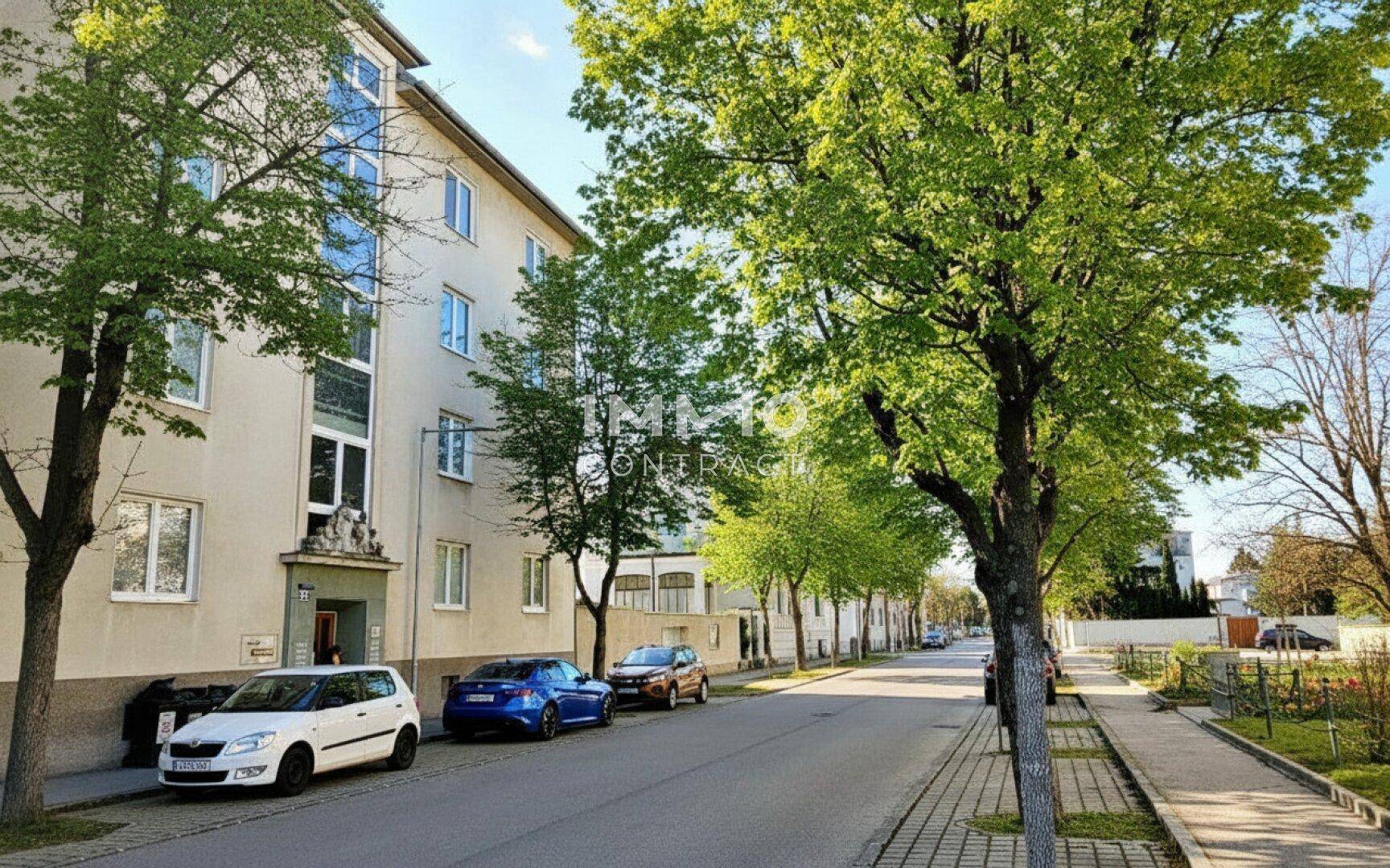 Mehrfamilienhaus mit grüner Umgebung, Balkonen und parkenden Autos an einer ruhigen Straße.