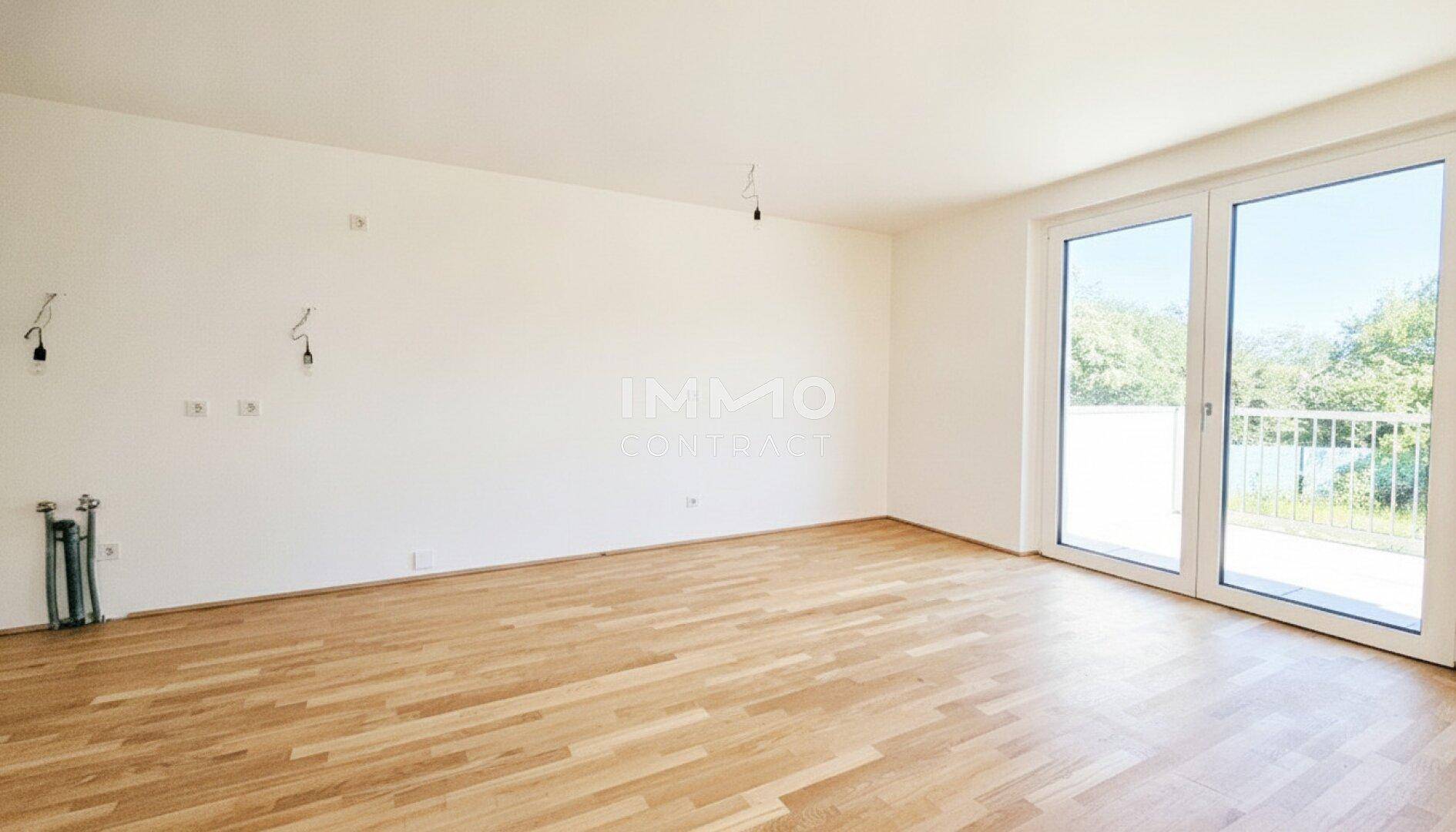 Geräumiges, leeres Zimmer mit hellem Parkettboden und Zugang zum Außenbereich.