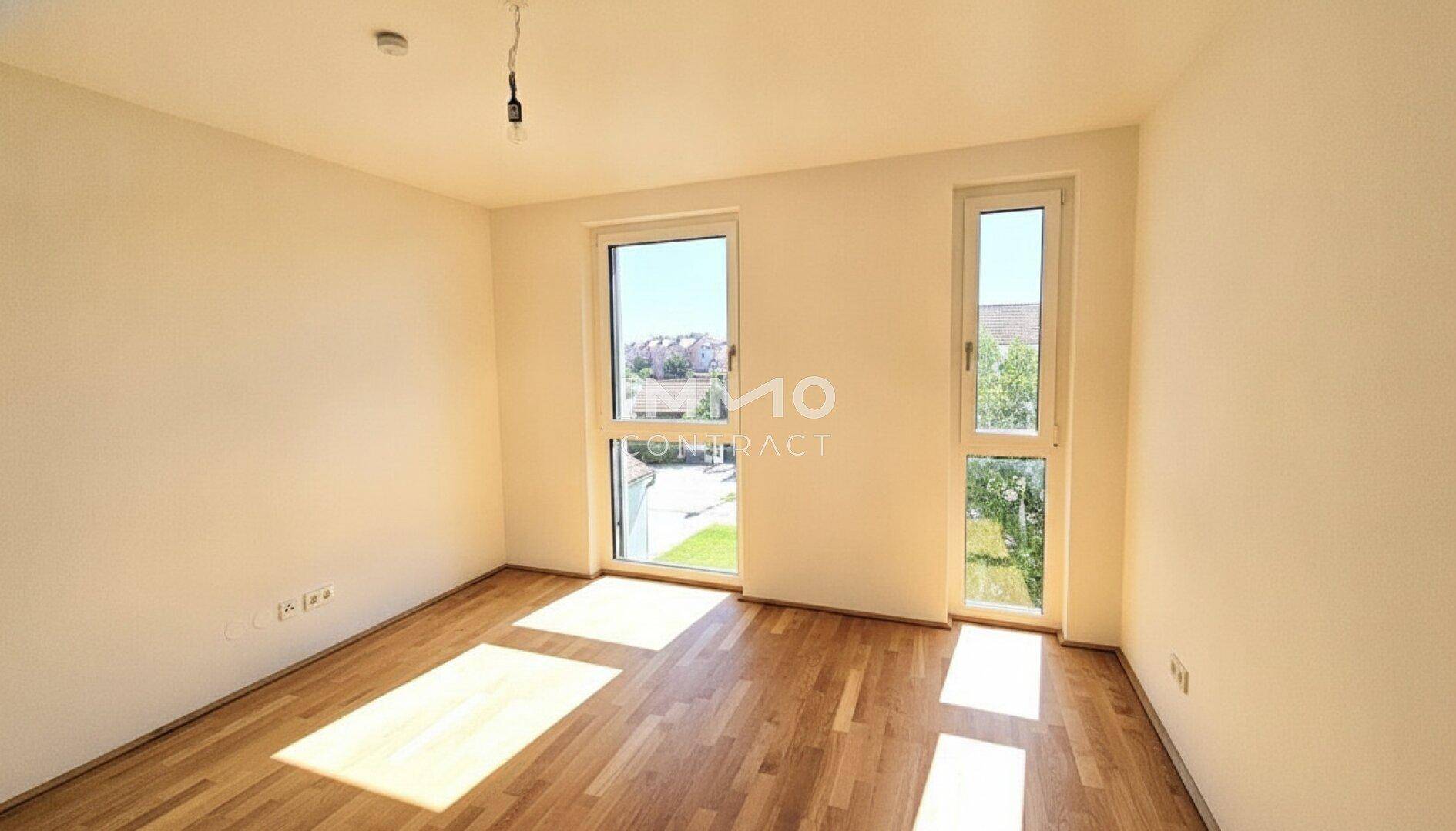 Sonniges Schlafzimmer mit Parkettboden und zwei großen Fenstern.