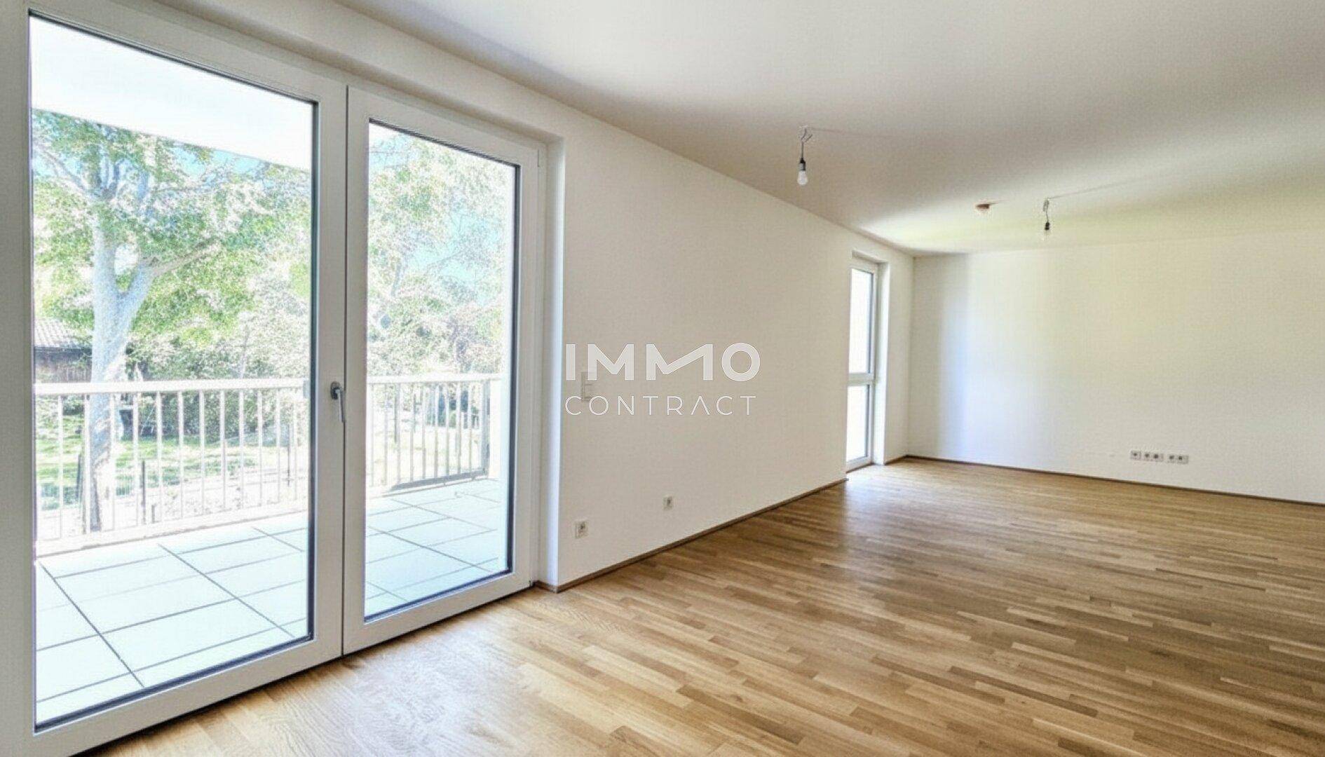 Geräumiges, leeres Wohnzimmer mit Parkettboden und großen Fenstertüren zum Balkon.