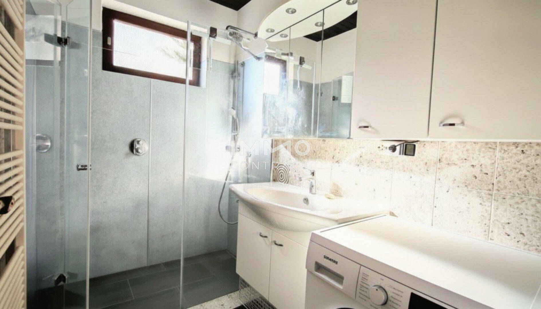 Modernes Badezimmer mit begehbarer Dusche, Waschbecken, Spiegelschrank und Waschmaschine.