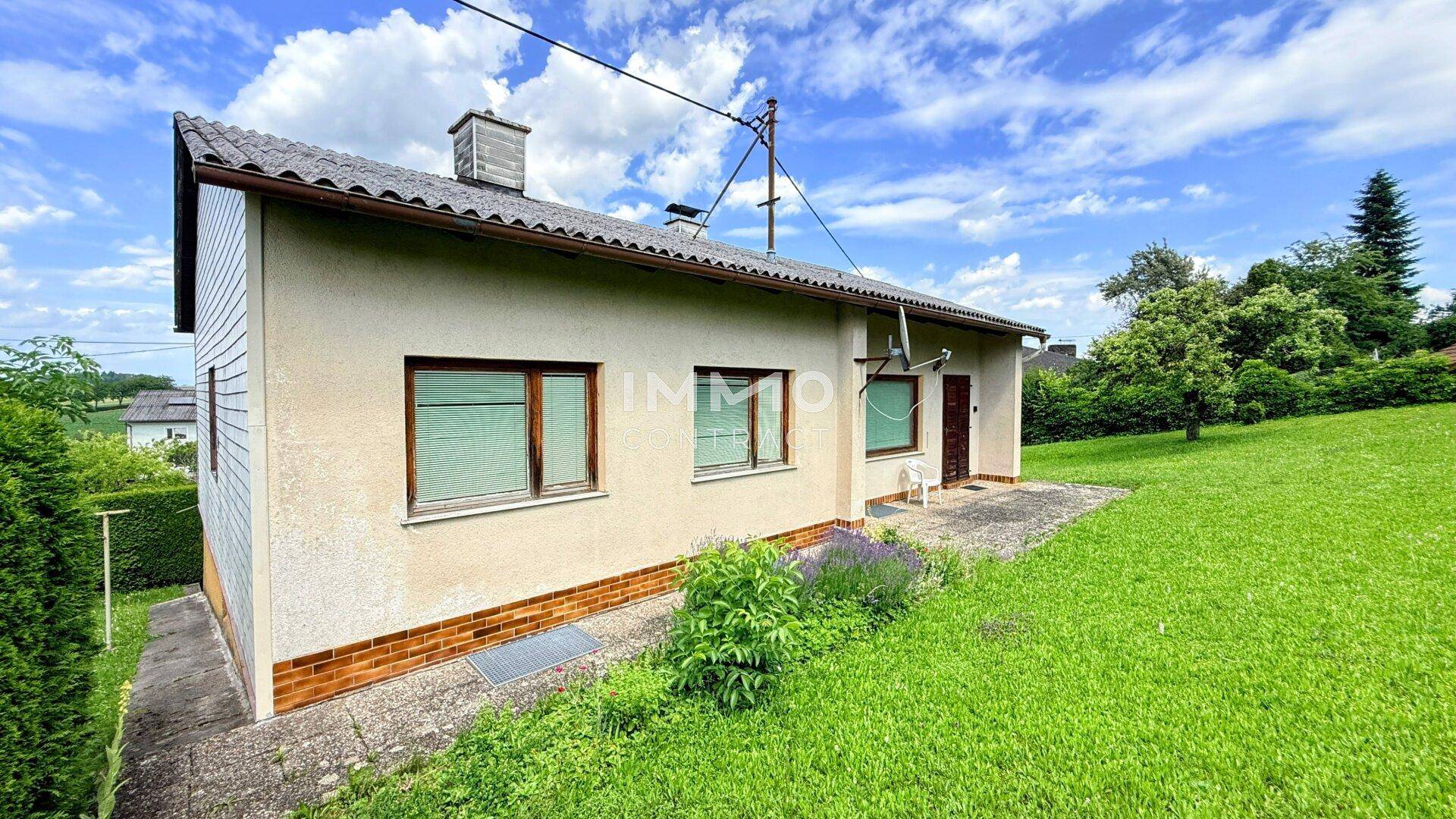 Seitenansicht des Hauses mit beiger Fassade, kleinen Fenstern und einem gepflasterten Bereich.