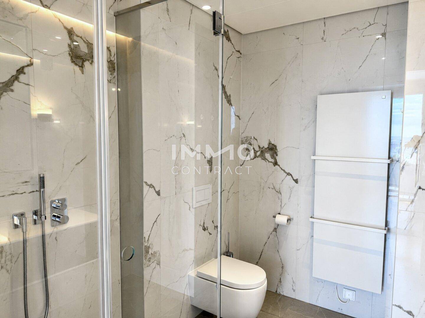 Modernes Badezimmer mit Marmorfliesen, begehbarer Dusche und wandhängendem WC sowie Handtuchheizkörper.
