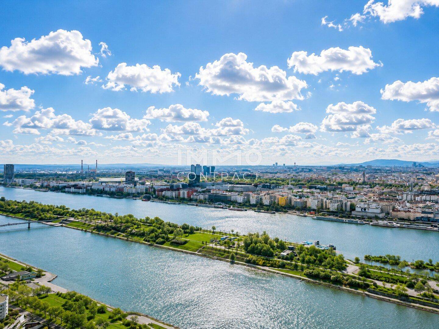 Weitläufige Luftaufnahme einer Stadtlandschaft mit einem Fluss und grünen Inseln unter blauem Himmel.