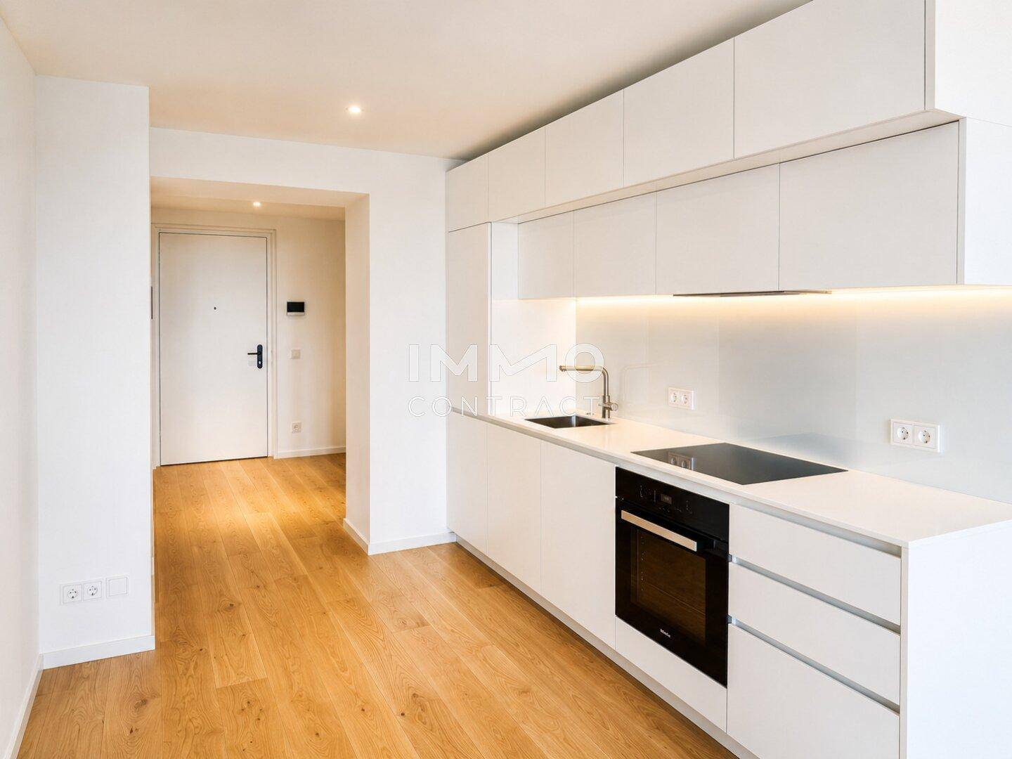 Moderne, weiße Einbauküche mit integrierten Geräten und Holzboden in einem offenen Wohnbereich.