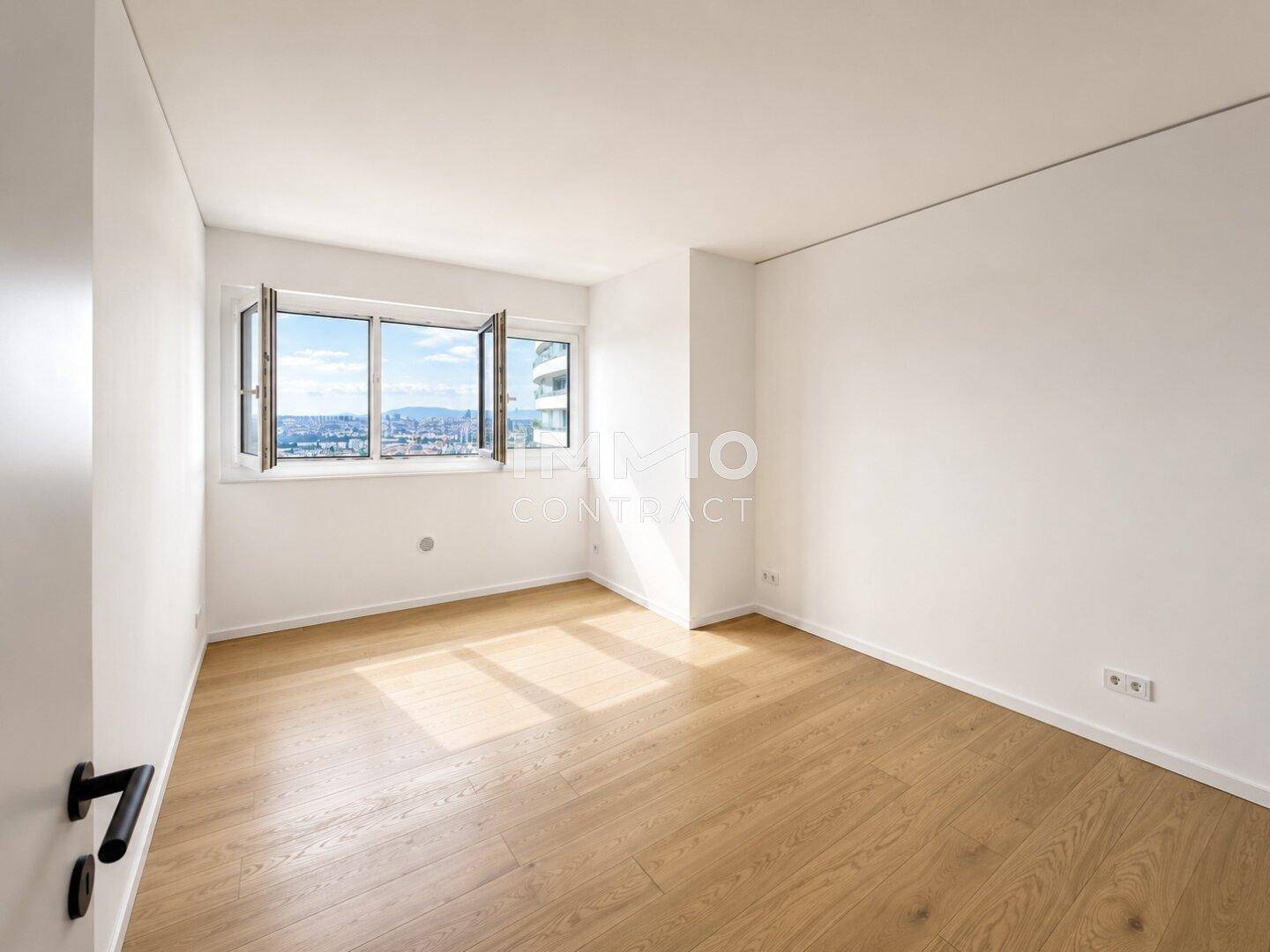 Helles, leeres Schlafzimmer mit Holzboden und Fenstern mit Stadt- und Flussblick.
