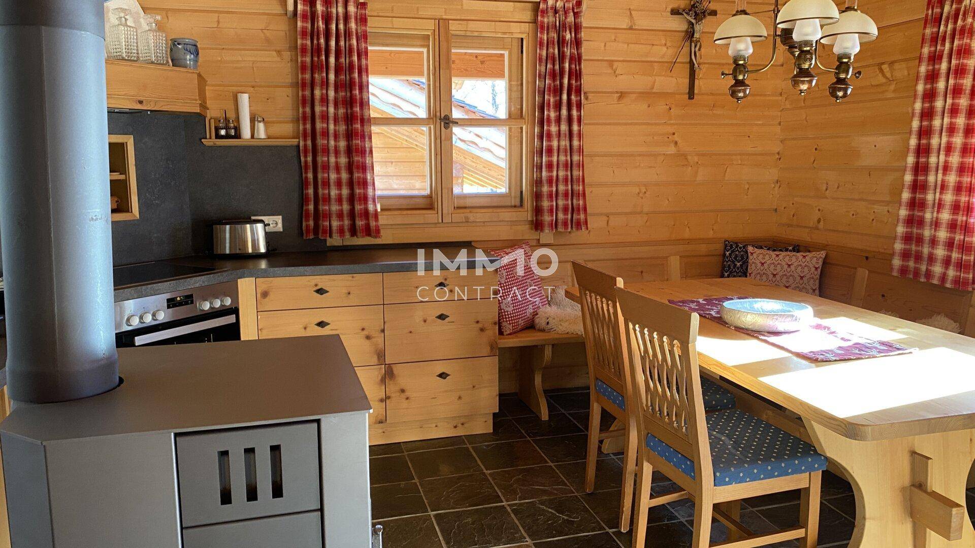 Gemütliche Wohnküche im Landhausstil mit Holzwänden, Essbereich und einem traditionellen Ofen.