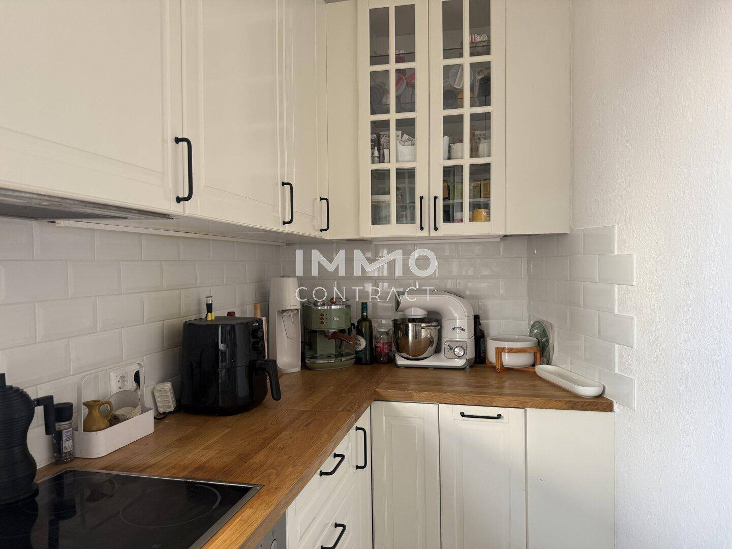 Detailansicht einer Küche mit weißen Schränken, Holztheke und modernen Küchengeräten.