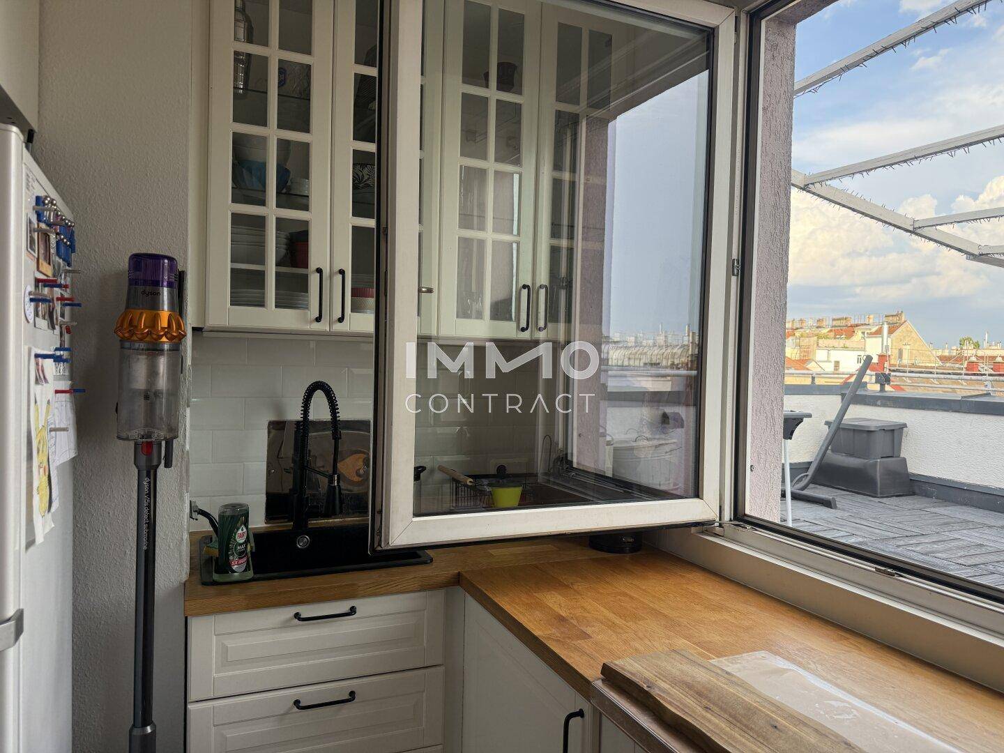 Helle Küche mit weißen Schränken, Holztheke und Fenster mit Blick auf die Dachterrasse.