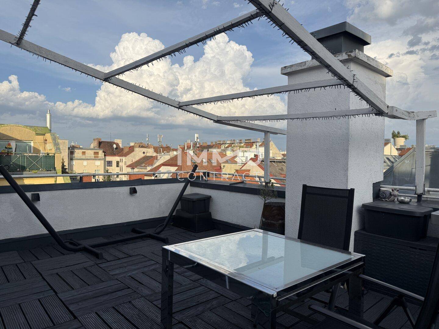 Weitläufige Dachterrasse mit dunklem Bodenbelag, Pergola und Blick über die umliegenden Dächer.