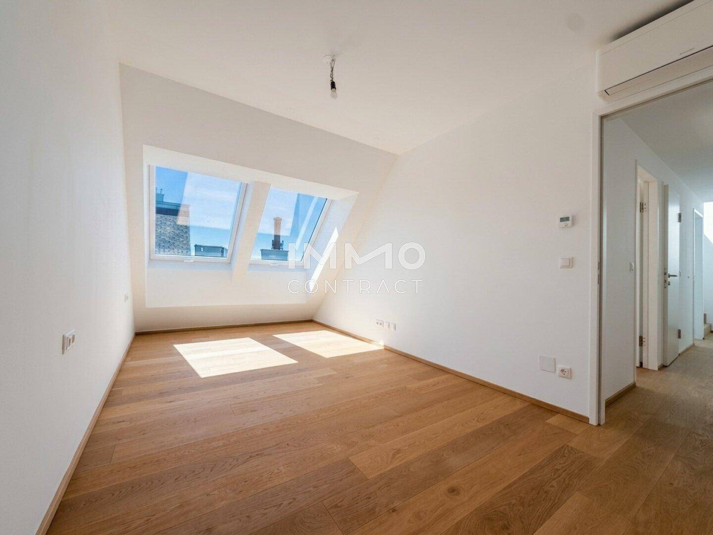 Geräumiges Zimmer mit Holzboden, Dachschrägen, Dachfenstern und Klimaanlage.