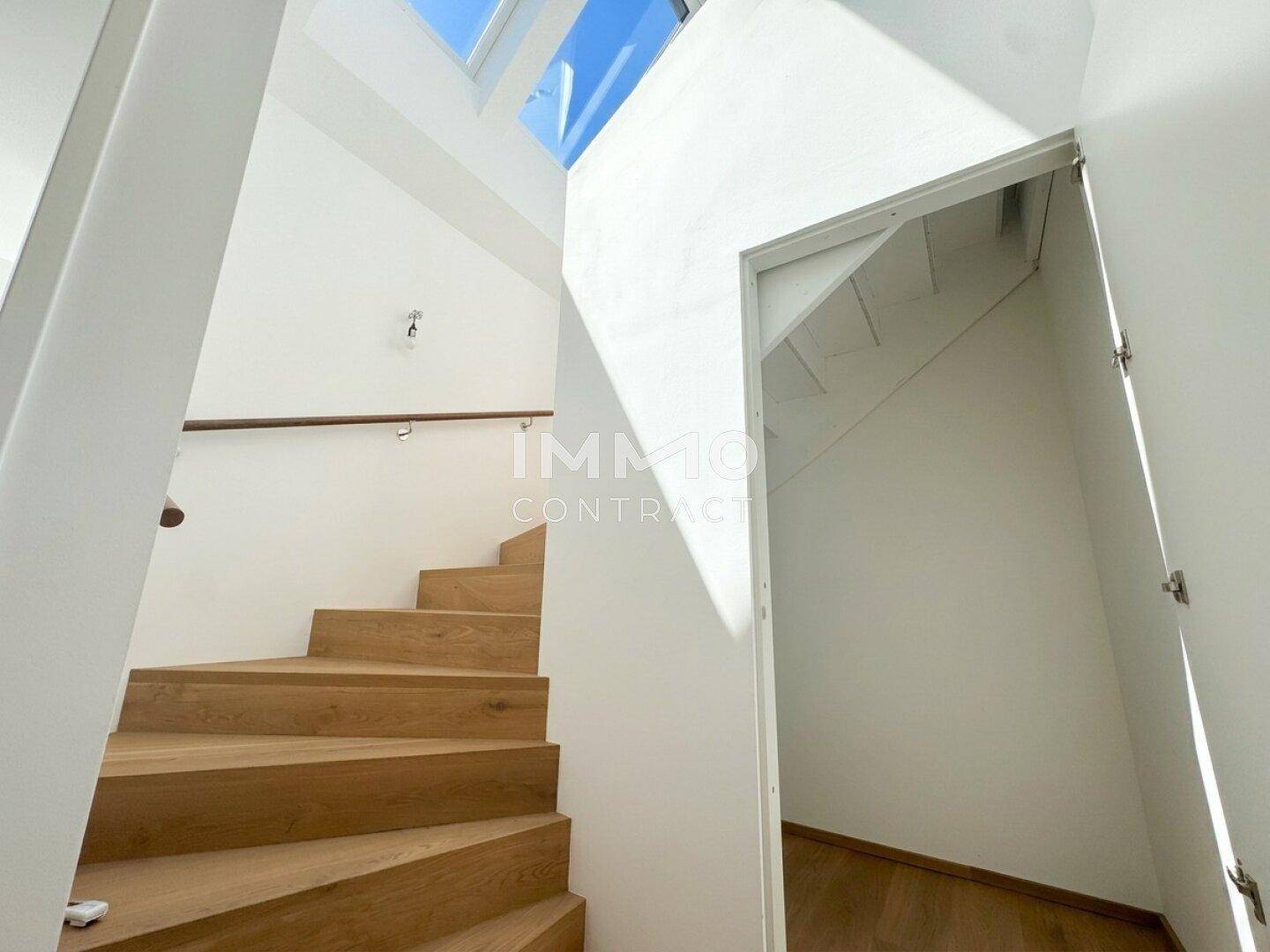 Heller Treppenaufgang mit Holzstufen und Handlauf, beleuchtet durch ein großes Dachfenster.