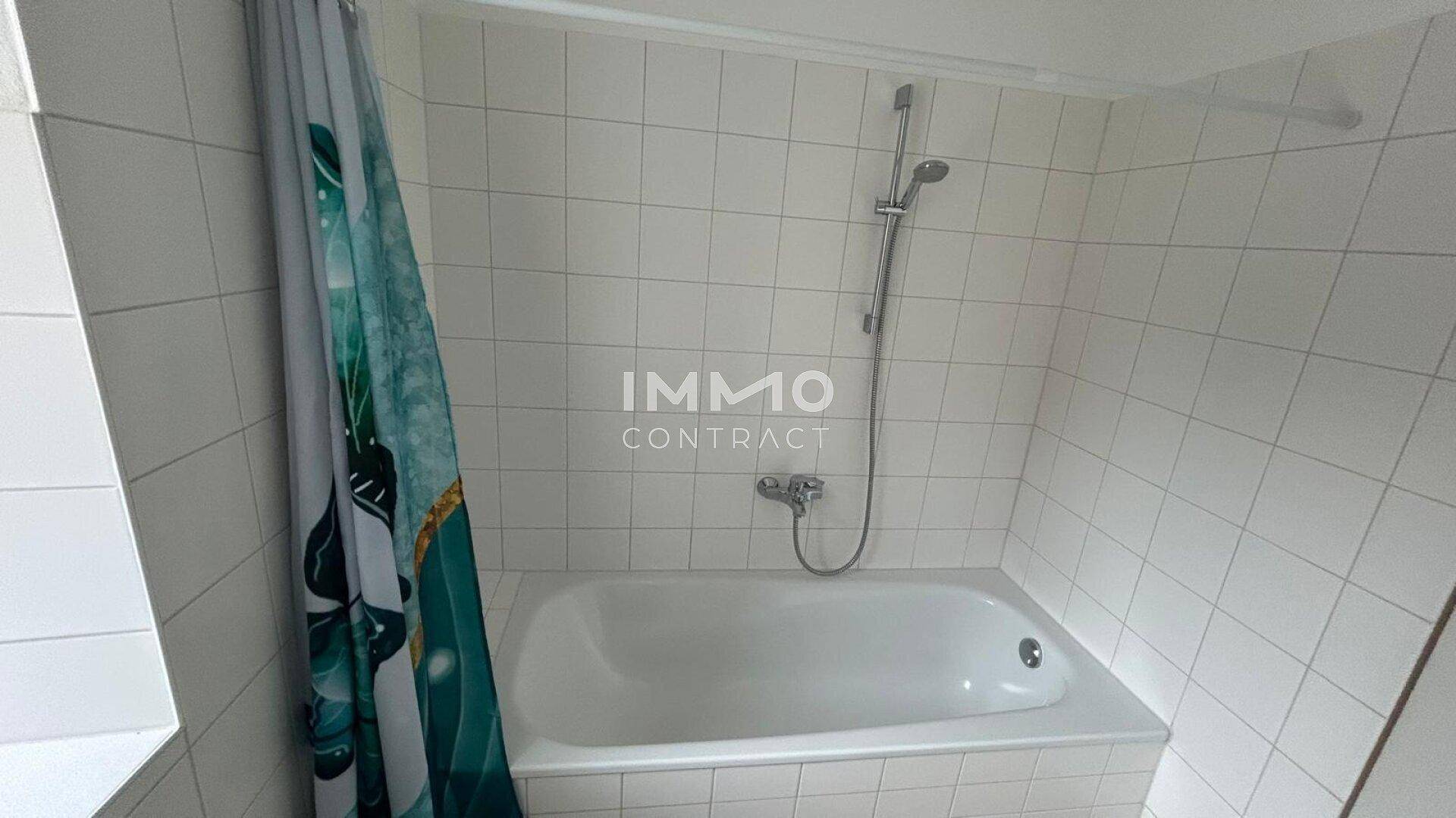 Badezimmer mit Badewanne und Duschvorhang, komplett gefliest in hellem Weiß.