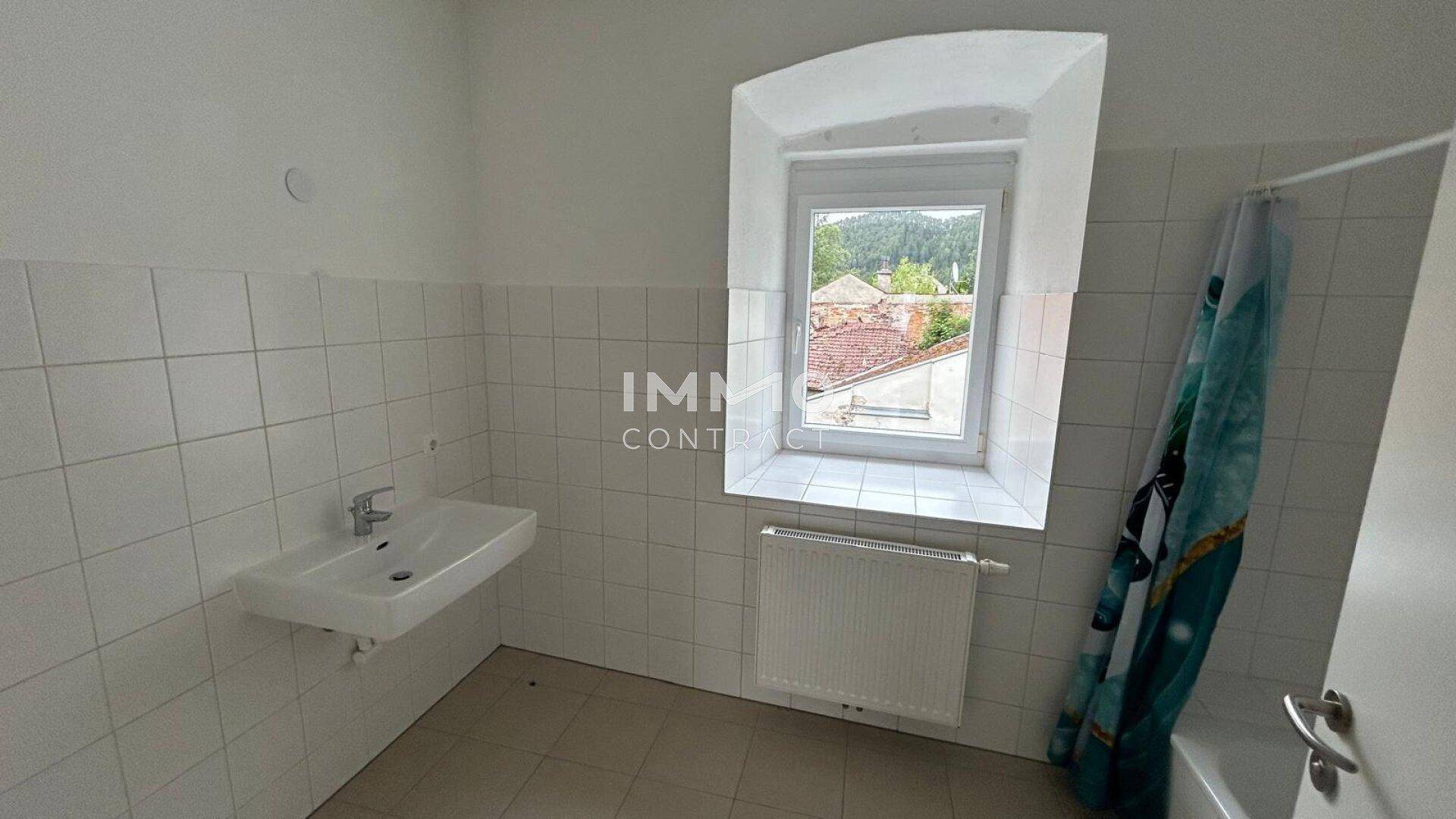 Helles Badezimmer mit Badewanne, Waschbecken und Fenster mit Ausblick auf die Umgebung.