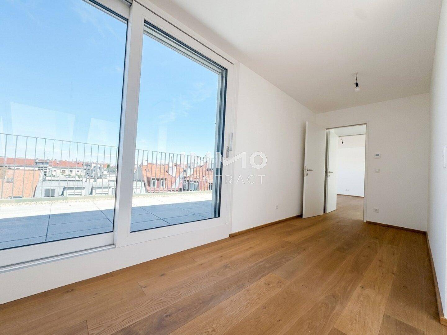 Geräumiges Zimmer mit Holzboden und bodentiefen Fenstern, die Zugang zur Terrasse bieten.