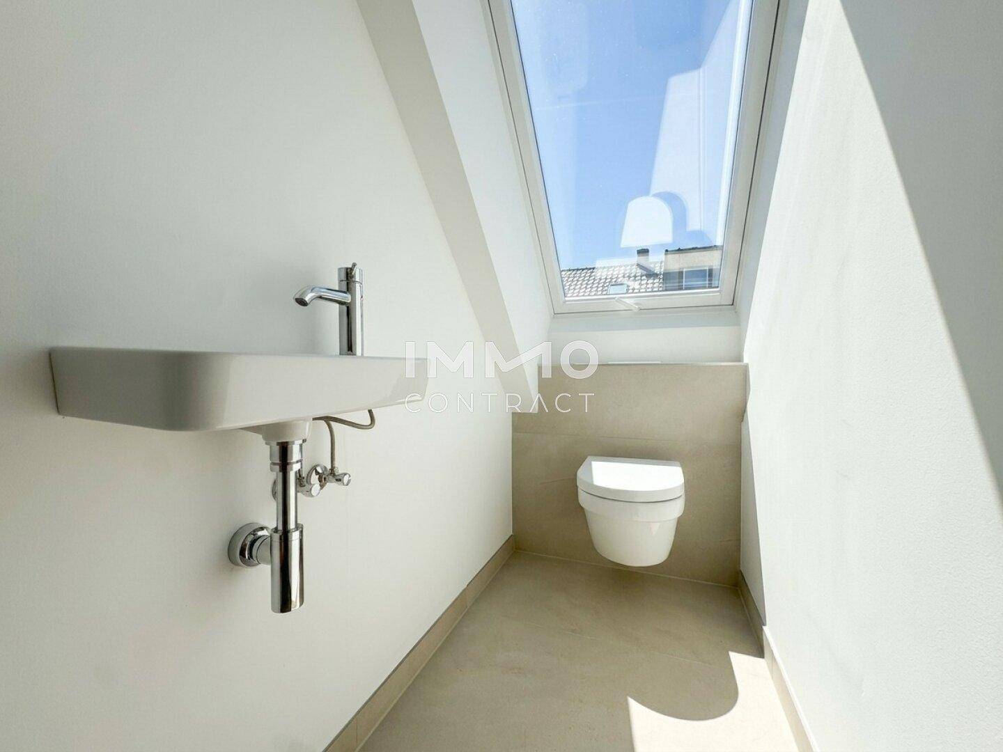 Helles Gäste-WC mit wandmontierter Toilette, Waschbecken und Dachfenster.