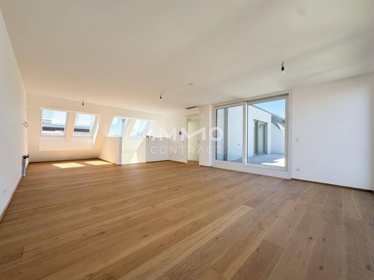 Geräumiges Wohnzimmer mit Holzboden, Dachschrägen und Zugang zu einer Terrasse.