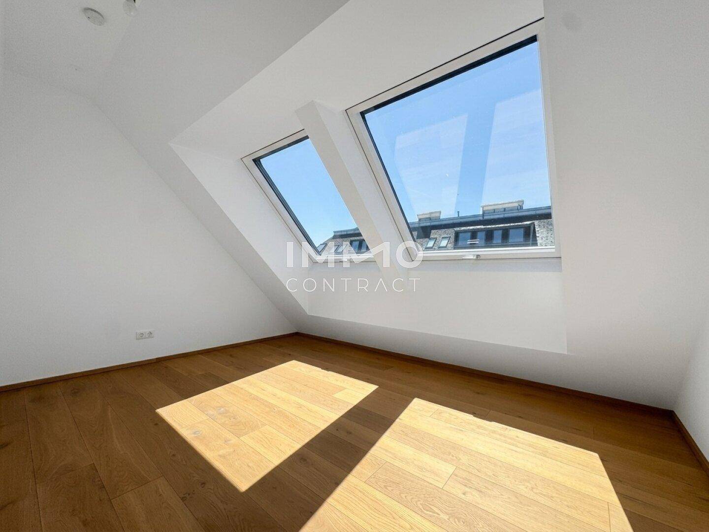 Helles Zimmer mit Holzboden und zwei Dachfenstern, die viel Tageslicht spenden.