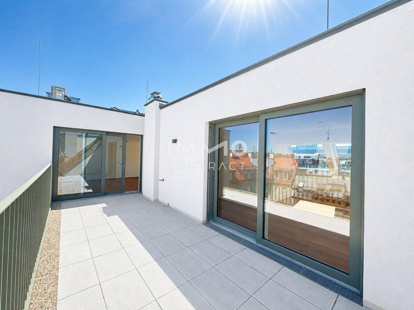 Sonnige Dachterrasse mit Fliesenboden und Zugang zu Innenräumen durch große Schiebetüren.