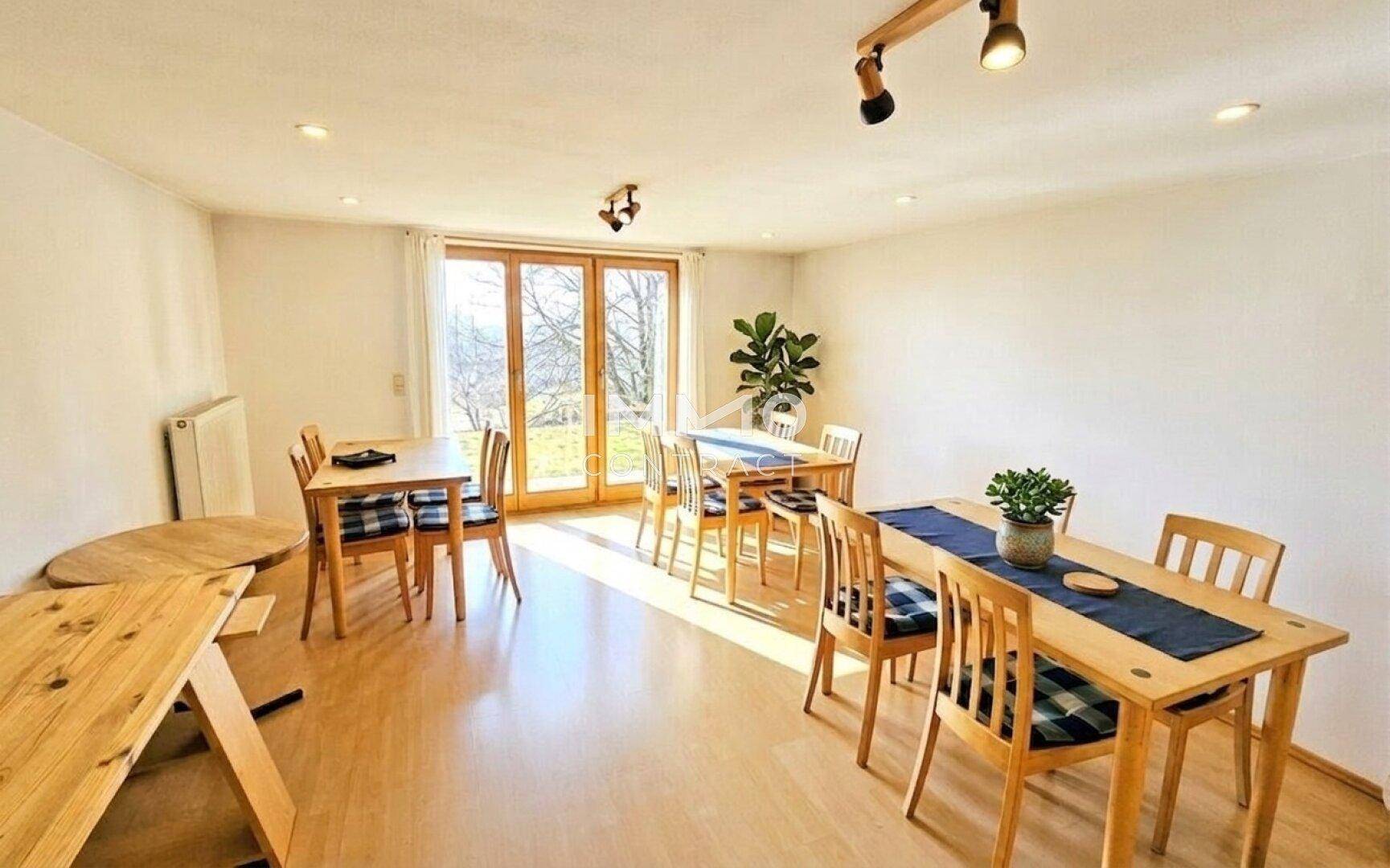 Heller Essbereich mit mehreren Holztischen und Zugang zu einem Außenbereich.