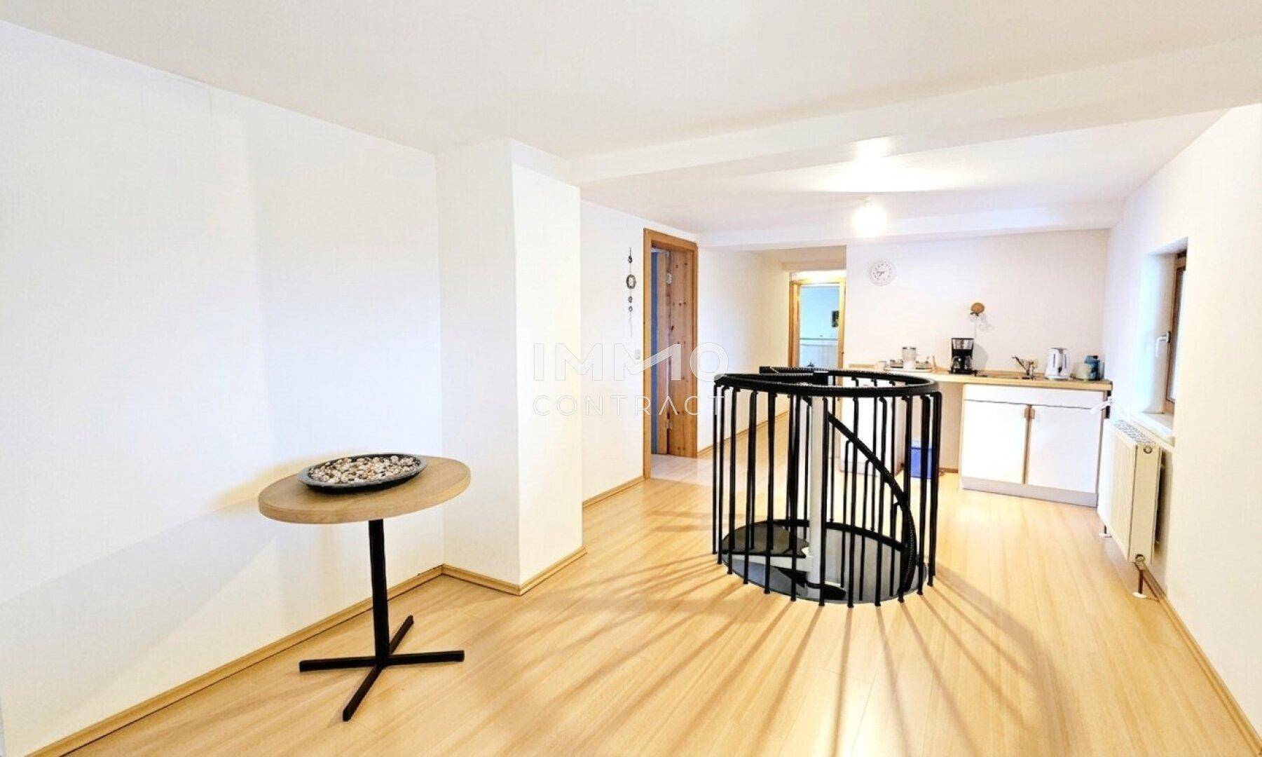 Offener Wohnbereich mit Wendeltreppe, kleiner Küchenzeile und Laminatboden.