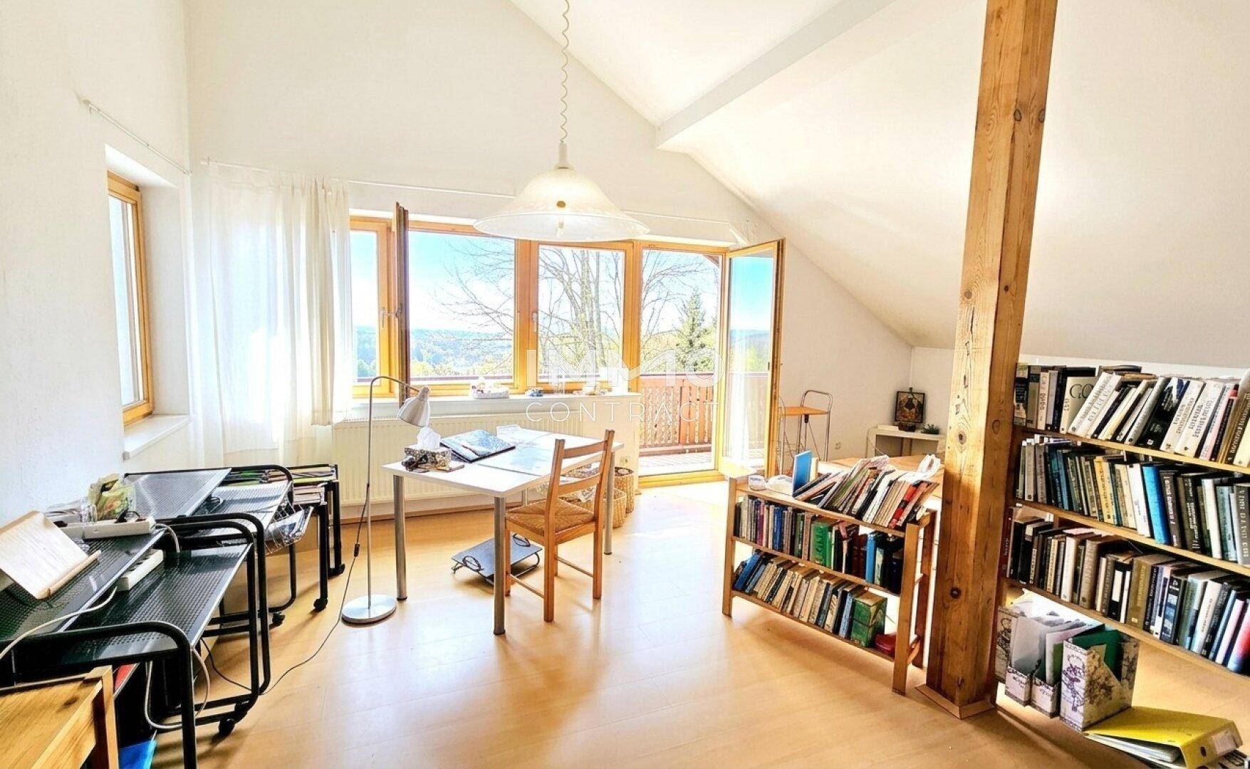 Helles Dachzimmer mit Bücherregalen, Schreibtisch und Zugang zu einem Balkon mit Weitblick.