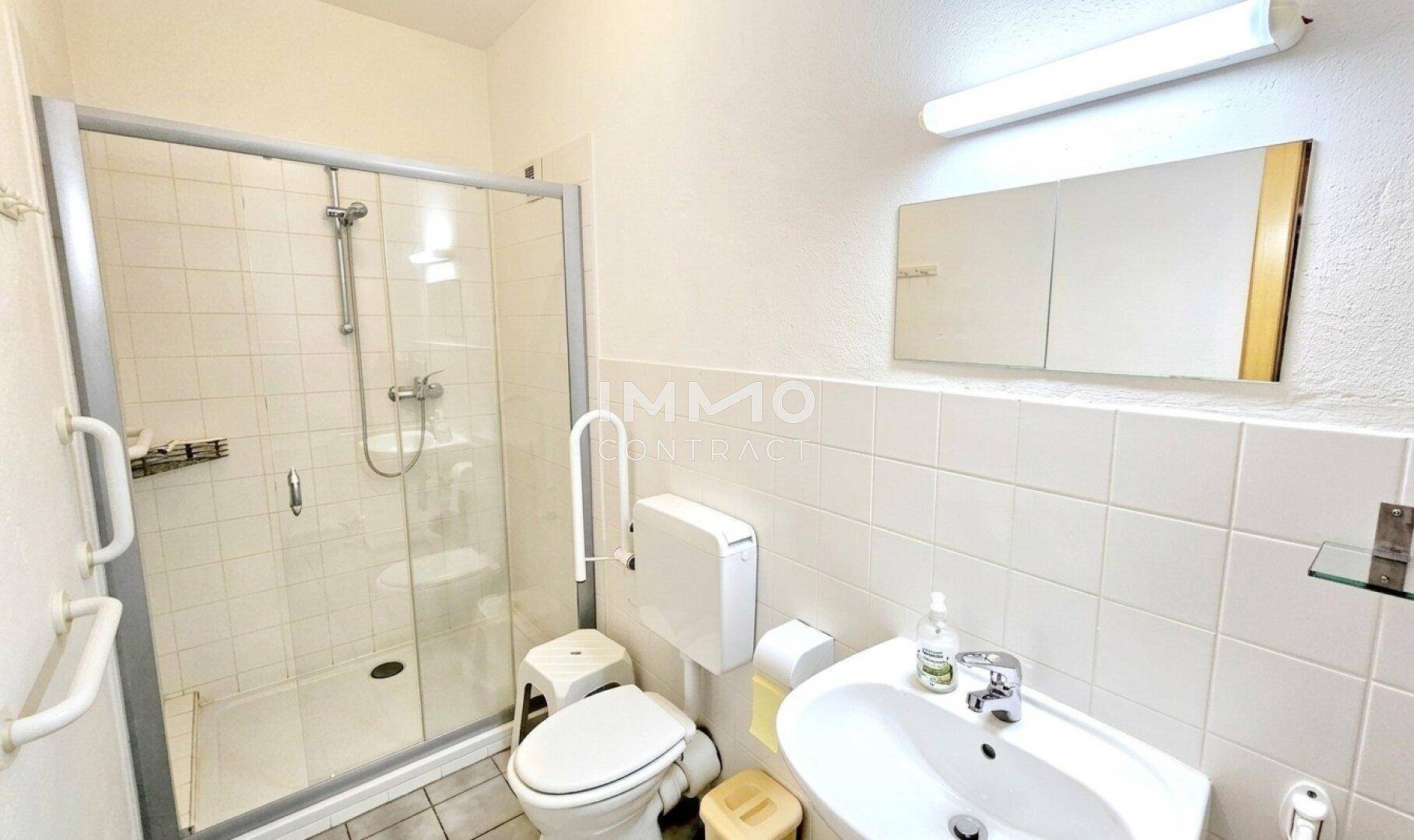 Barrierefreies Badezimmer mit Dusche, WC und Haltegriffen für zusätzliche Sicherheit.