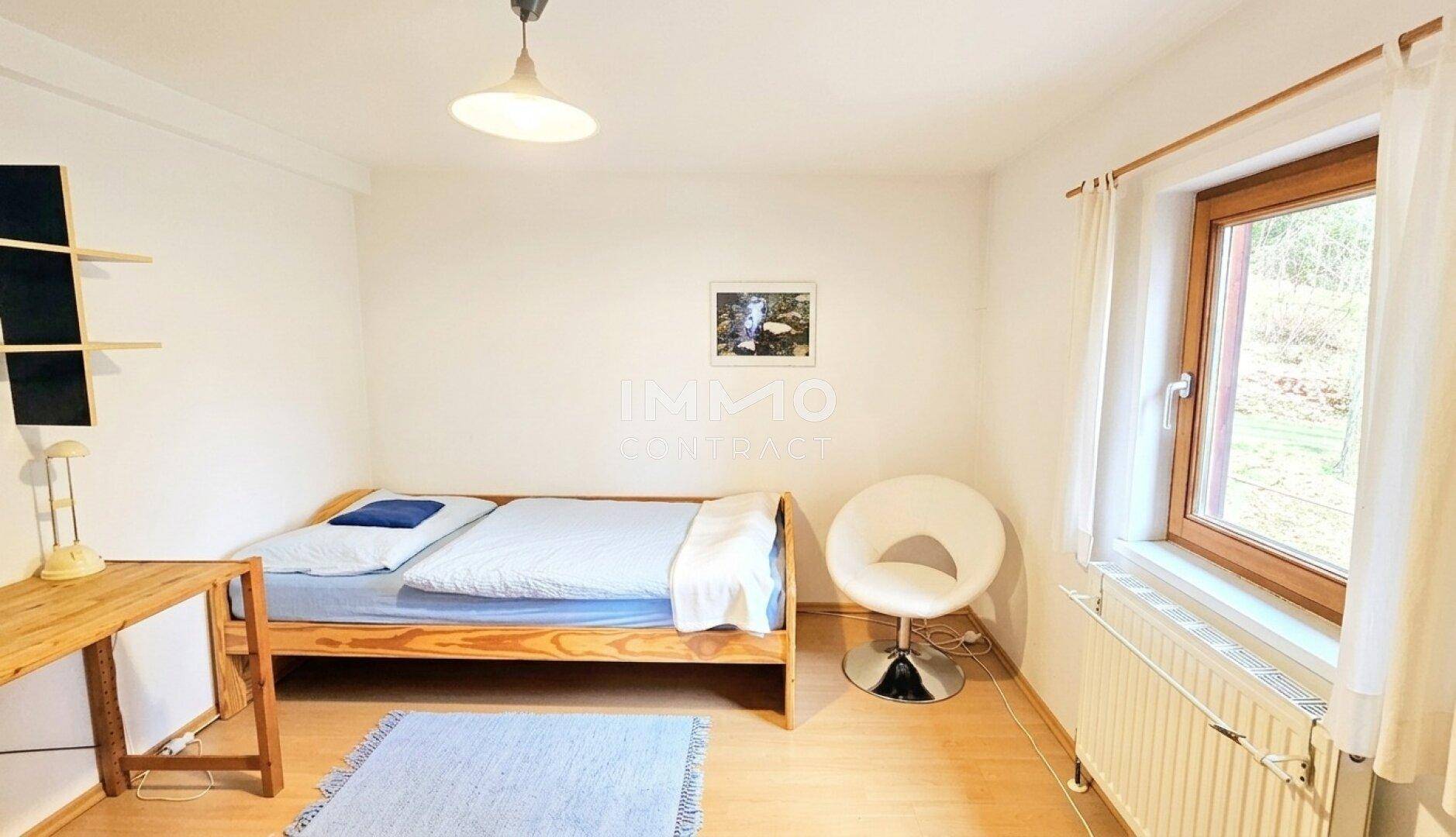 Schlichtes Schlafzimmer mit Einzelbett, Schreibtisch und Blick ins Grüne.