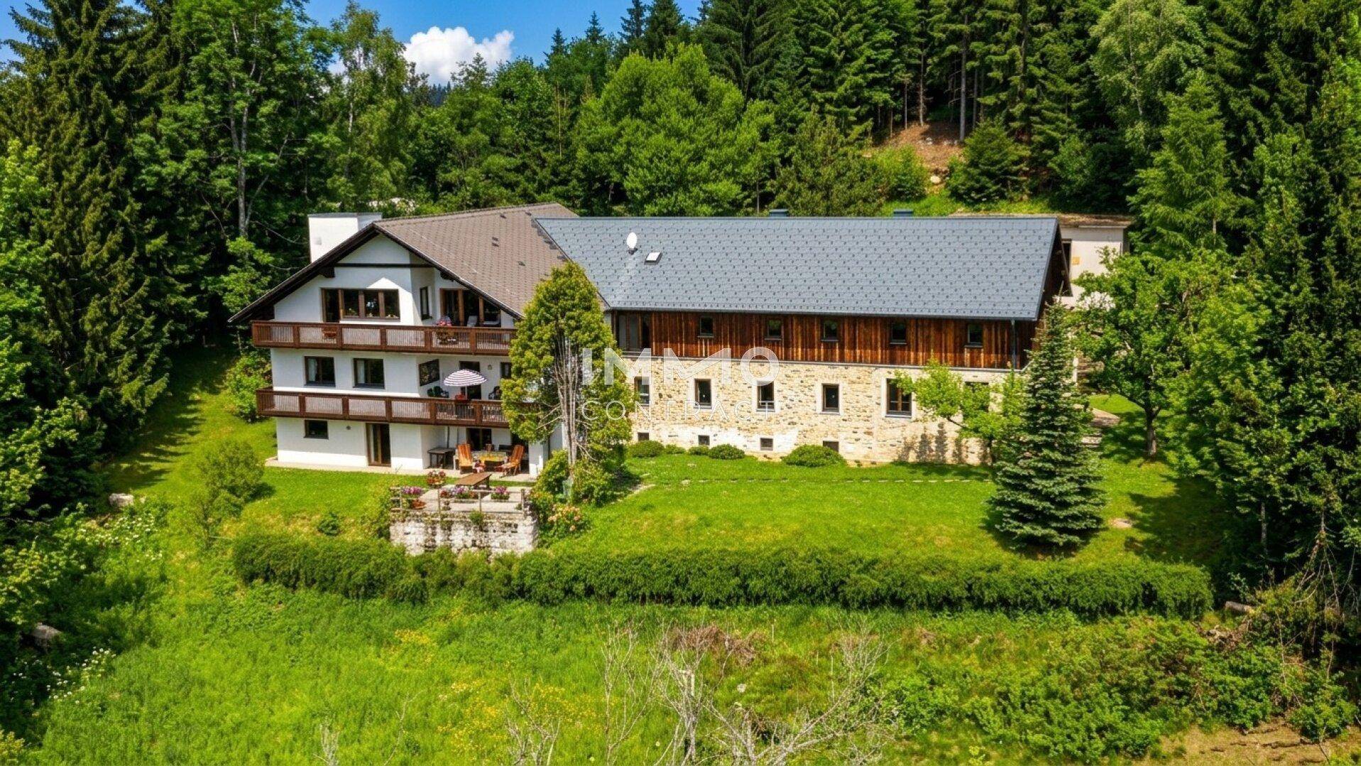 Weitläufiges Anwesen mit mehreren Gebäudeteilen, umgeben von Wald und grünen Wiesen.