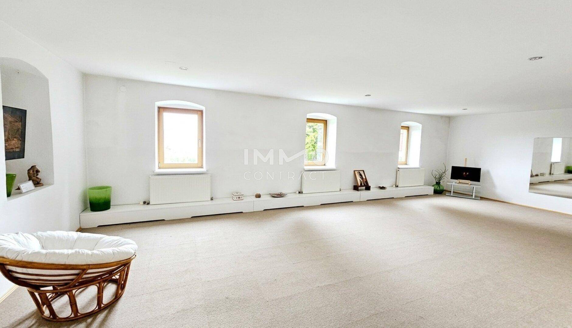 Heller, geräumiger Raum mit Teppichboden, großen Fenstern und minimalistischer Einrichtung.