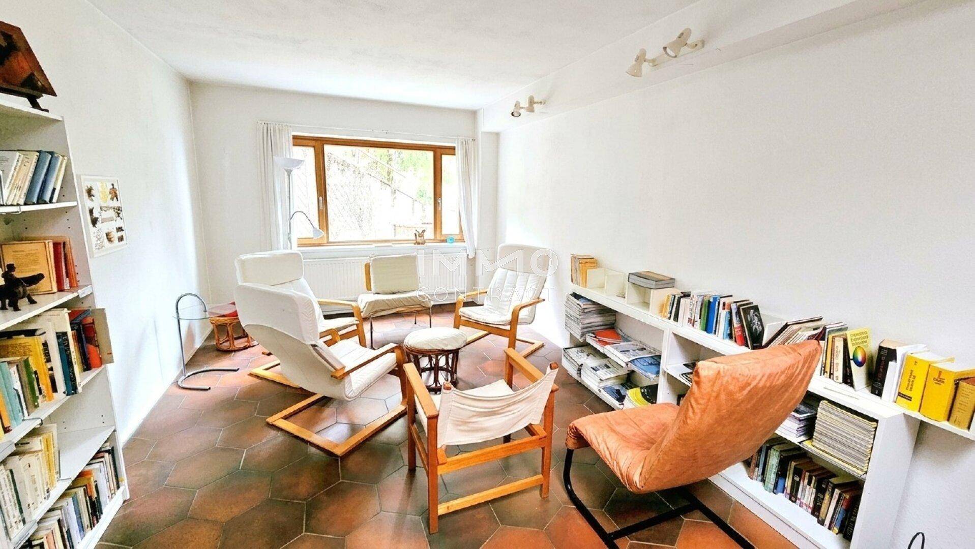 Gemütlicher Wohnraum mit Bücherregalen, bequemen Sesseln und Terrakotta-Fliesenboden.