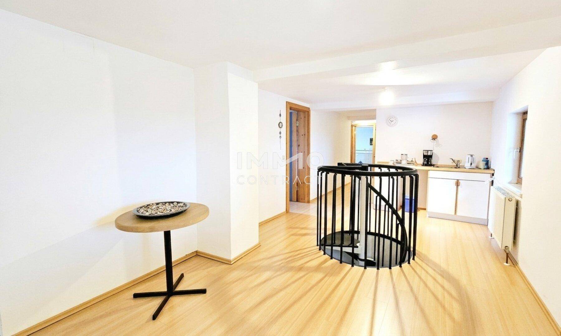 Offener Wohnbereich mit Wendeltreppe, kleiner Küchenzeile und hellem Laminatboden.