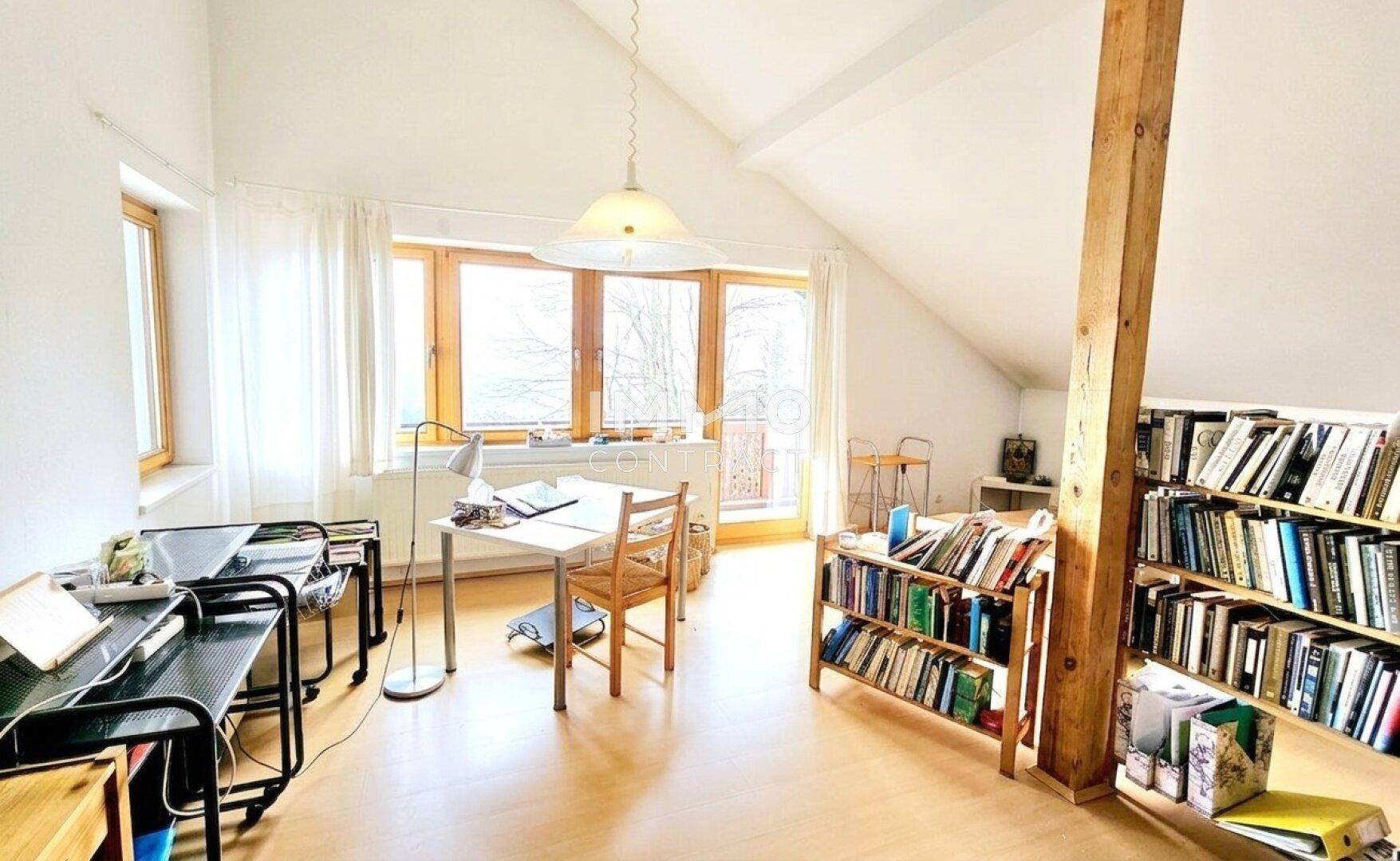 Helles Dachzimmer mit Schreibtisch, Bücherregalen und Zugang zu einem Balkon mit Weitblick.