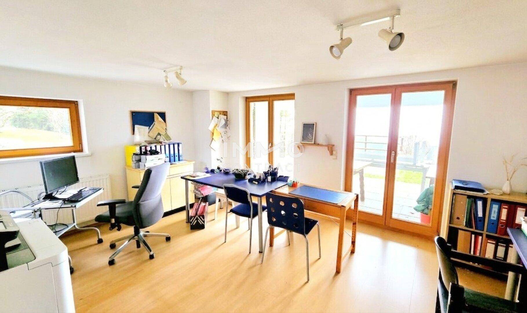 Heller Büroraum mit mehreren Arbeitsplätzen, großen Fenstern und Zugang zum Außenbereich.