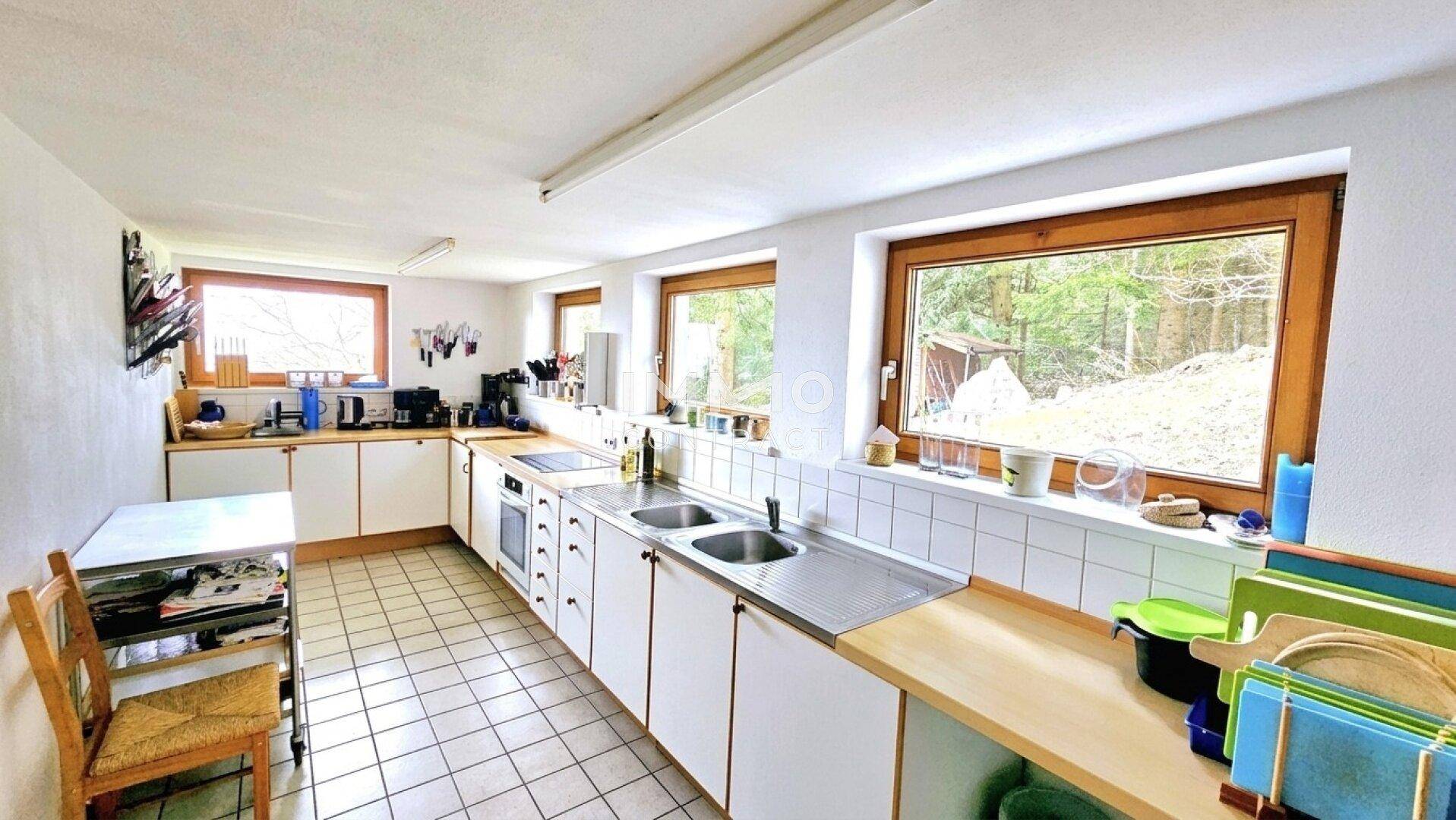 Funktionale Küche mit weißen Schränken, Fliesenboden und Blick ins Grüne.