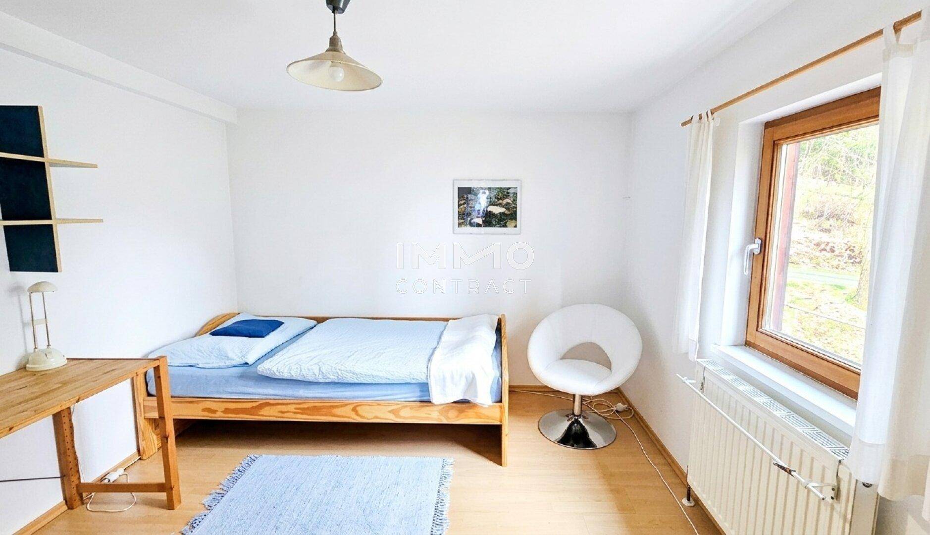 Helles Schlafzimmer mit Einzelbett, Schreibtisch und Laminatboden.
