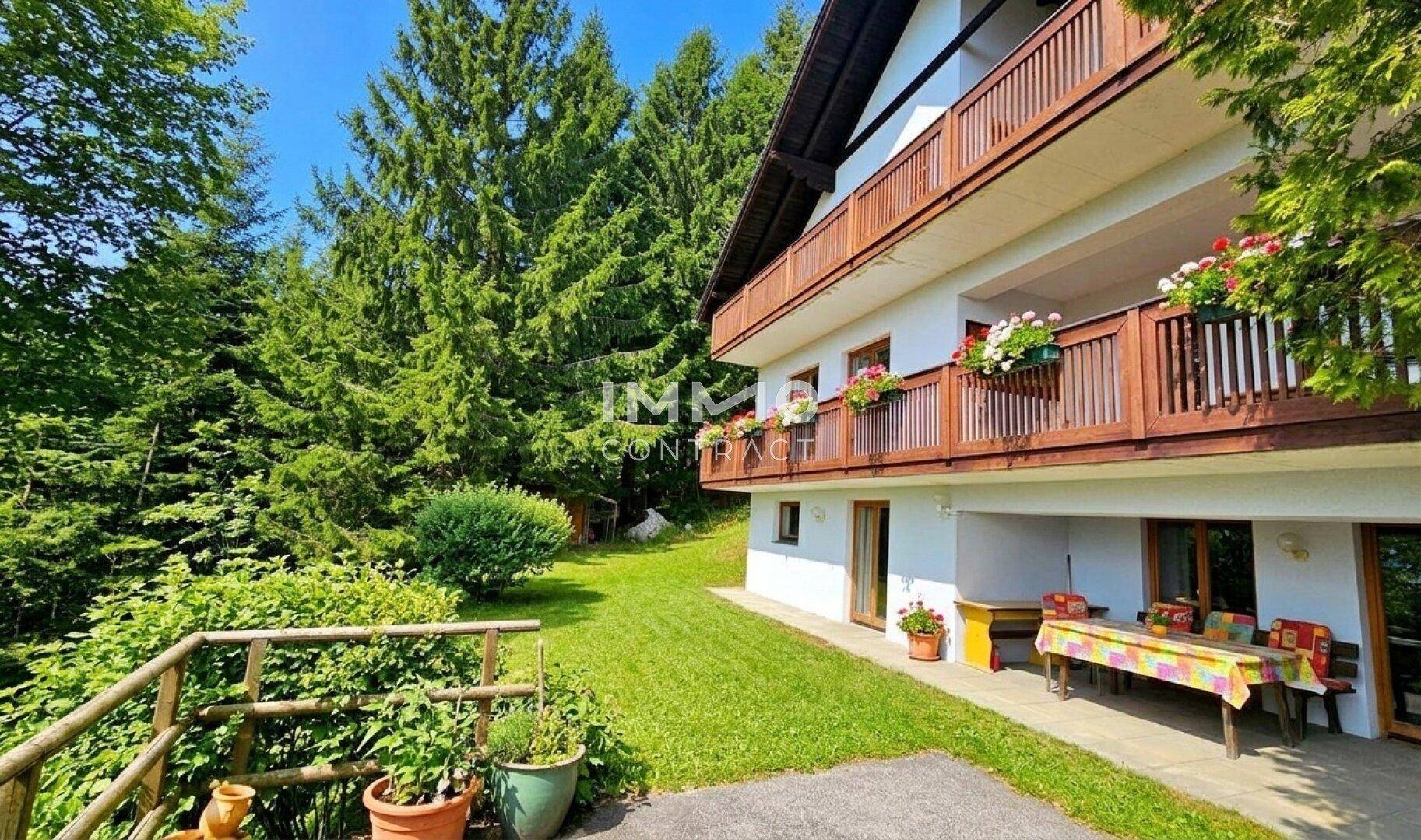 Gemütliche Terrasse mit Esstisch und Blumenkästen, umgeben von grüner Natur und Bäumen.