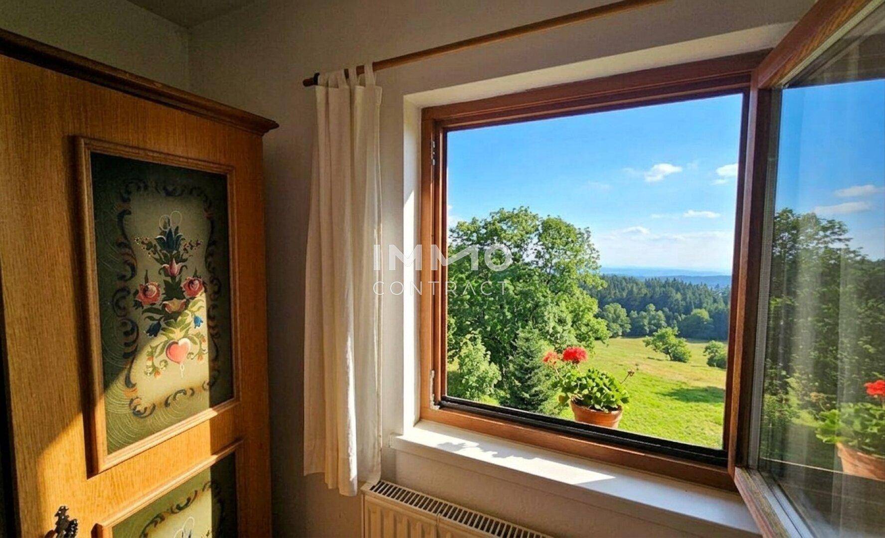 Fensterblick aus einem Zimmer auf die weite grüne Landschaft und den Horizont.