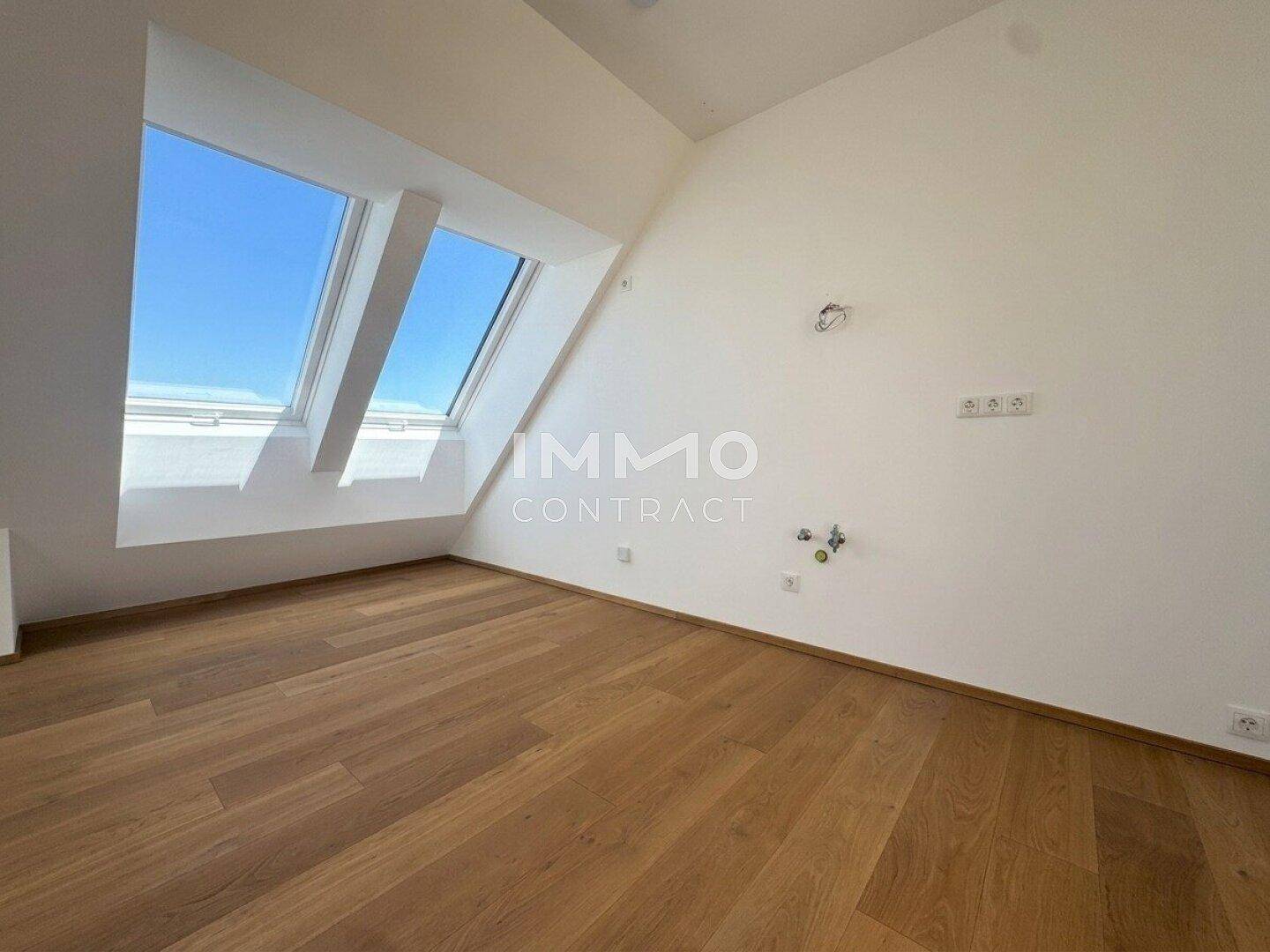 Helles Schlafzimmer mit Holzboden und schrägen Dachfenstern, die viel Sonnenlicht hereinlassen.