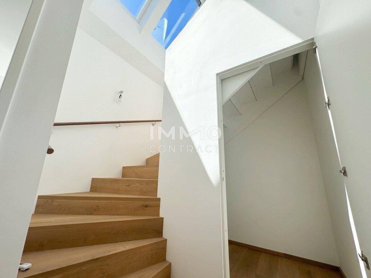 Helle Holztreppe mit Handlauf und Dachfenstern, die den Treppenaufgang erhellen.