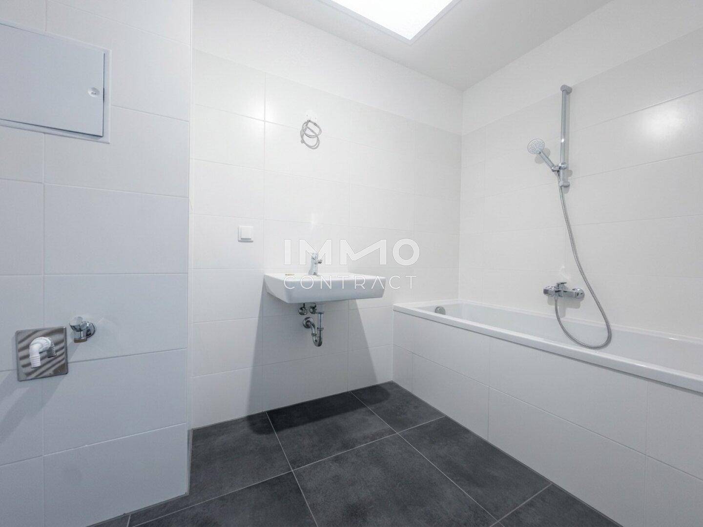 Modernes Badezimmer mit Badewanne, Waschbecken, weißen Wandfliesen und dunklem Boden.