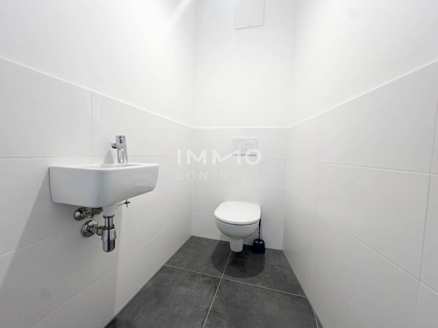 Modernes Gäste-WC mit wandhängender Toilette, kleinem Waschbecken und dunklen Bodenfliesen.