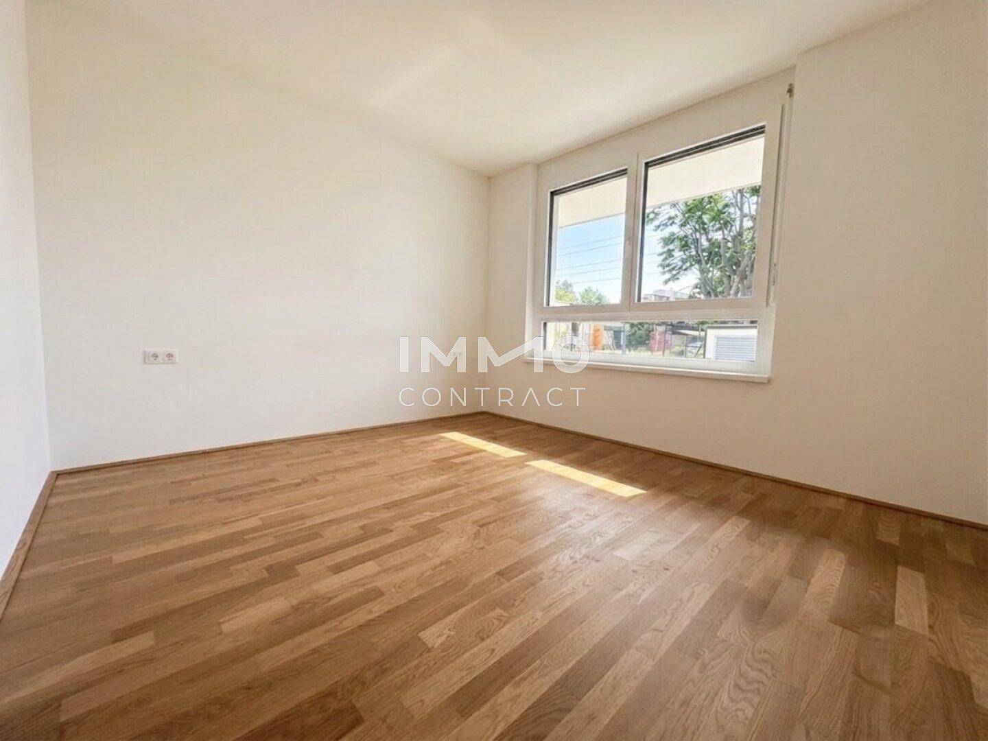 Helles Schlafzimmer mit Parkettboden und großem Fenster, das viel Tageslicht hereinlässt.