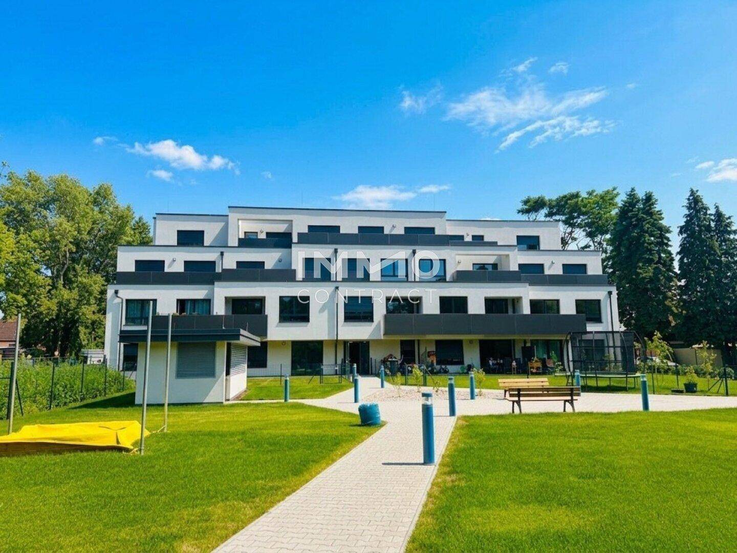 Rückansicht des modernen Gebäudes mit großem Gemeinschaftsgarten, Wegen und Spielbereich.