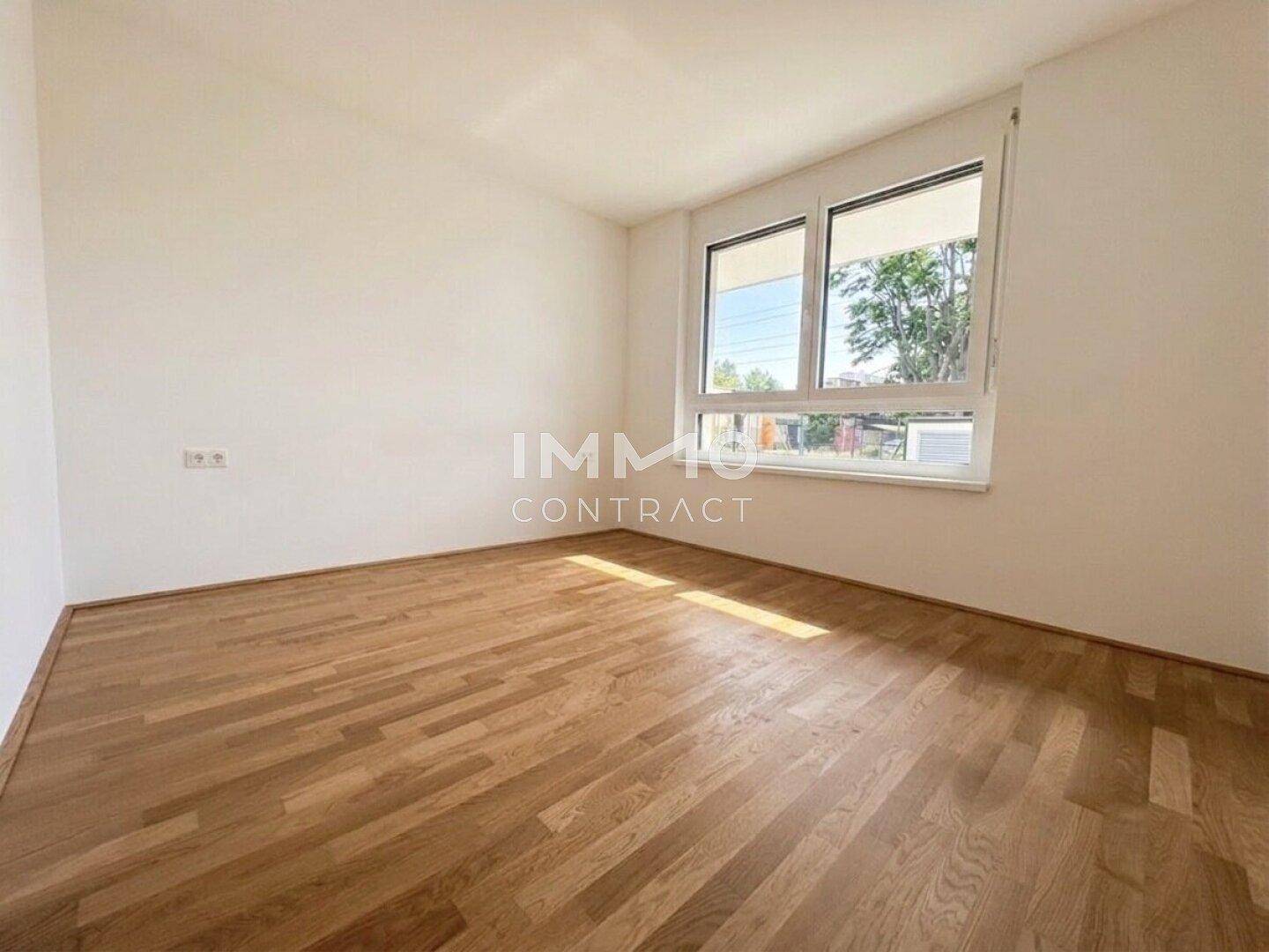 Schlafzimmer mit hellem Parkettboden und großem Fenster, das viel Tageslicht hereinlässt.